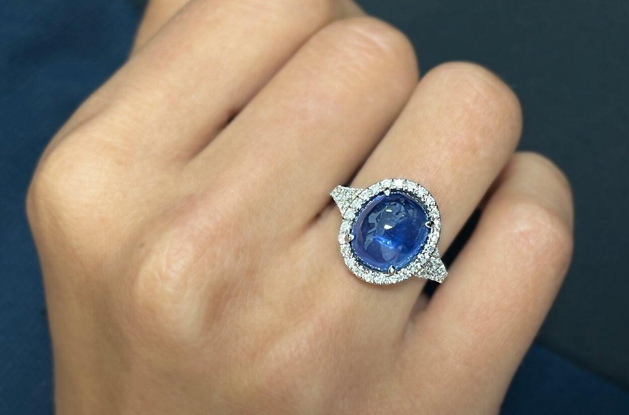 Allow me to introduce a remarkable 18kt white gold ring, adorned with a halo of dazzling diamonds encircling a GIA certified cabochon sapphire at its center. This ring is a testament to both opulence and refinement, a jewel that radiates beauty and