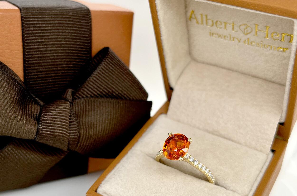 Elegance personified, this 18kt Yellow Gold Ring is a true treasure. At its heart lies a captivating oval mandarin garnet, a fiery gem that radiates warmth and allure. Embellishing the sides, a delicate trail of pave diamonds dances like starlight