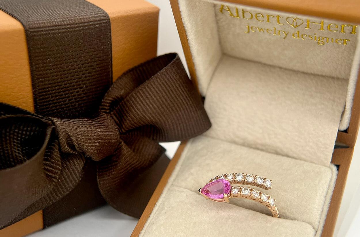 Introducing the Bypass Ring, a striking and unique piece of jewelry. Crafted in exquisite 18kt gold, this ring elegantly wraps around your finger, creating a captivating visual journey. At its heart, a pear-shaped pink sapphire, like a blooming bud,
