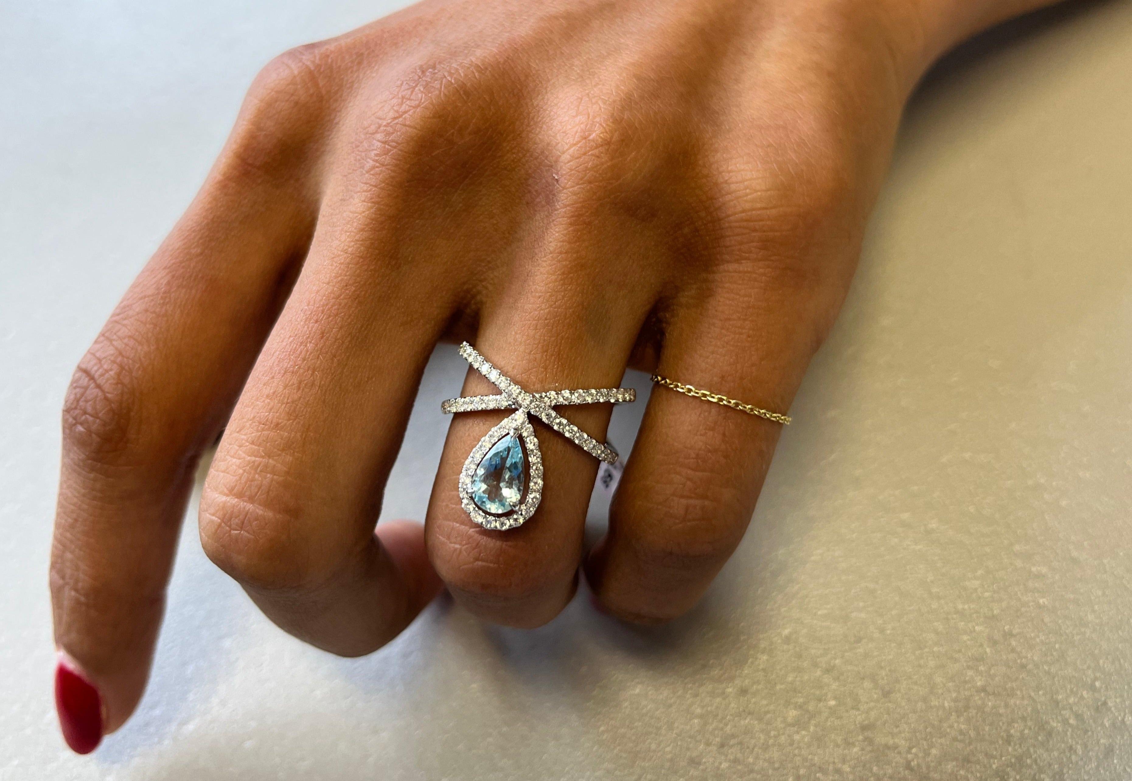Délicatement réalisée en or blanc 18kt, cette élégante bague présente une aigue-marine sereine de 0,68 carat entourée d'un gracieux motif croisé de 37 diamants étincelants (0,59 carat). Avec un poids de 5,4 grammes et une taille de 6,5, c'est une