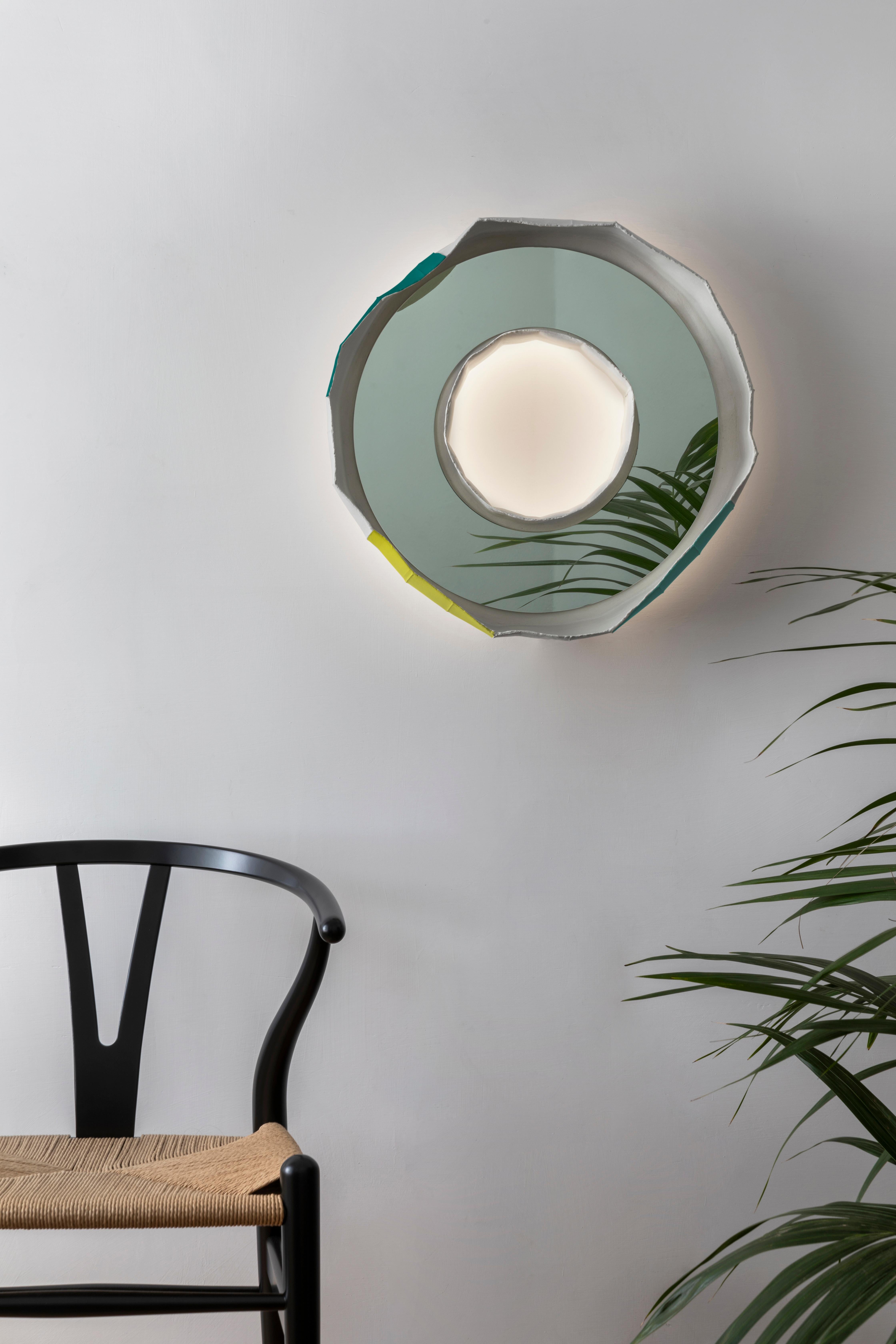 RING AURA, une étonnante lampe-miroir fabriquée à la main en Italie, l'un des 2 modèles qui composent la collection REFLECTIONS, fruit d'une collaboration entre l'artiste Paola Paronetto et le designer Giovanni Botticelli, qui intègre la céramique à