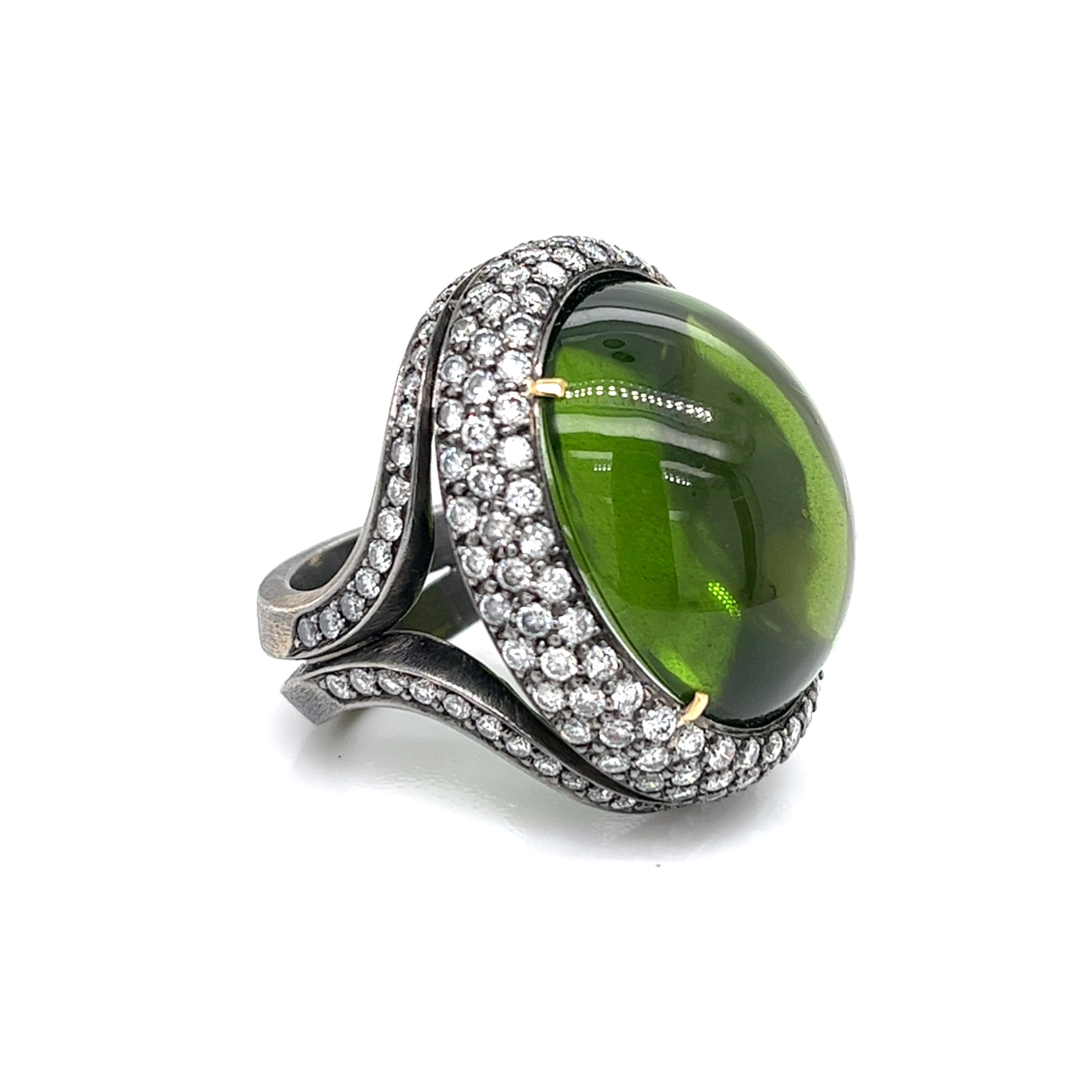 This exquisite piece features an 18kt white gold unique design with a striking black rhodium, with center showcasing a top-quality peridot in an oval cabochon cut. The gem is elegantly surrounded by 174 dazzling pave-set diamonds, creating a truly