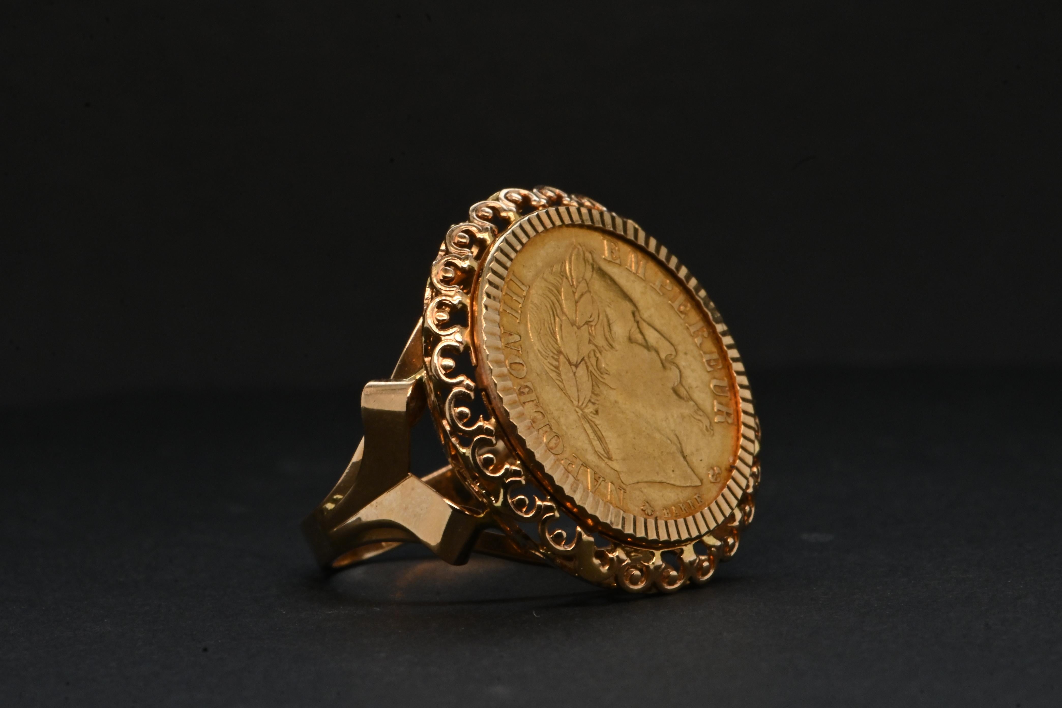 This exceptional 18-carat gold ring features an 1868 10 franc coin depicting Napoleon III. The coin, in 24-carat gold, features the emperor's profile crowned with laurels. 

The edge of the coin is delicately adorned with openwork gold lace, adding