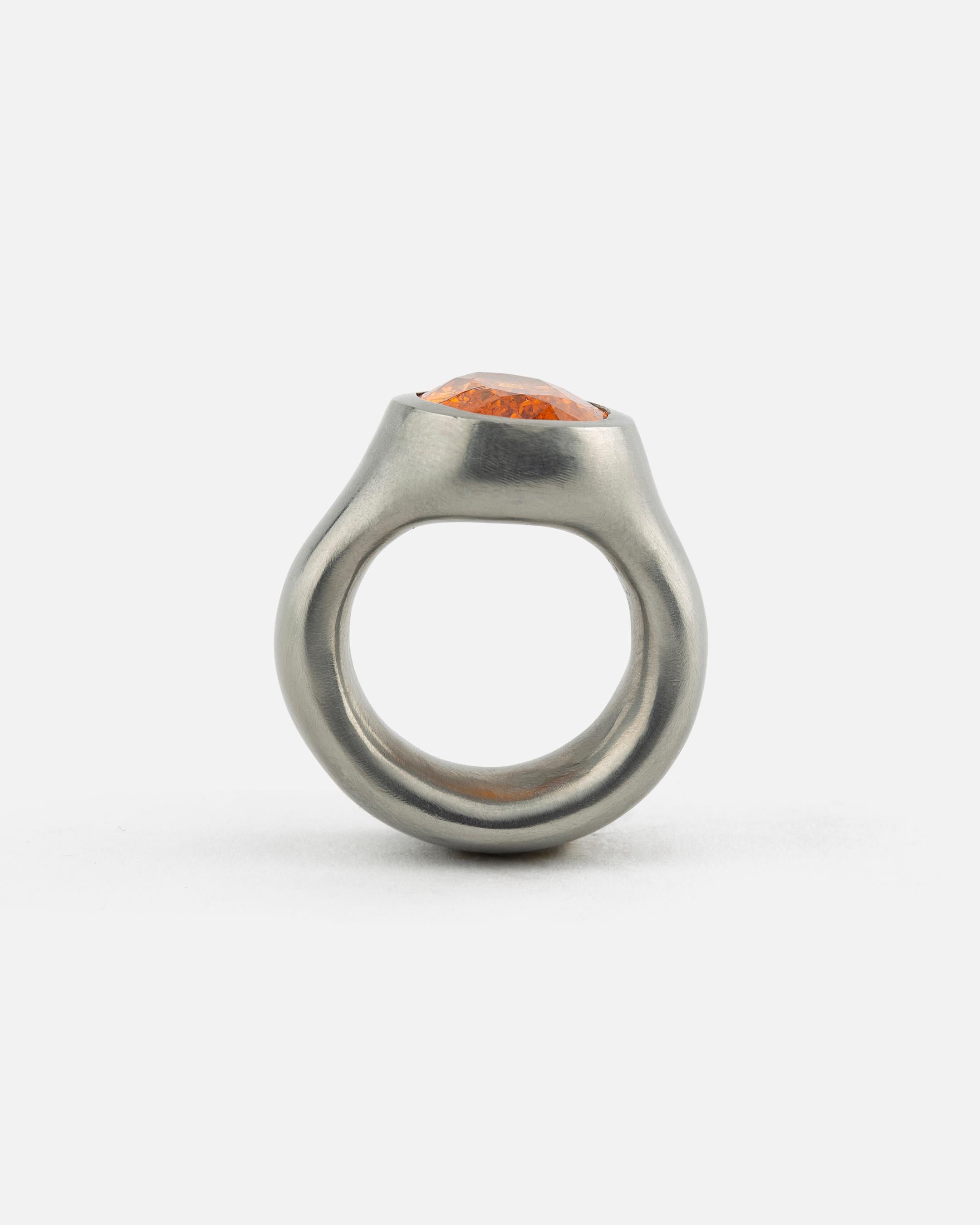 Dieser Ring ist aus einem Stück Hafnium geschnitzt. Der Stein ist ein Hessonit mit einer intensiven Farbe. 
Hergestellt von Peter Hassenpflug, dessen Schmuckstücke sich auf reine Elemente beschränken: Feingold, Feinsilber, Feinplatin, Kupfer,