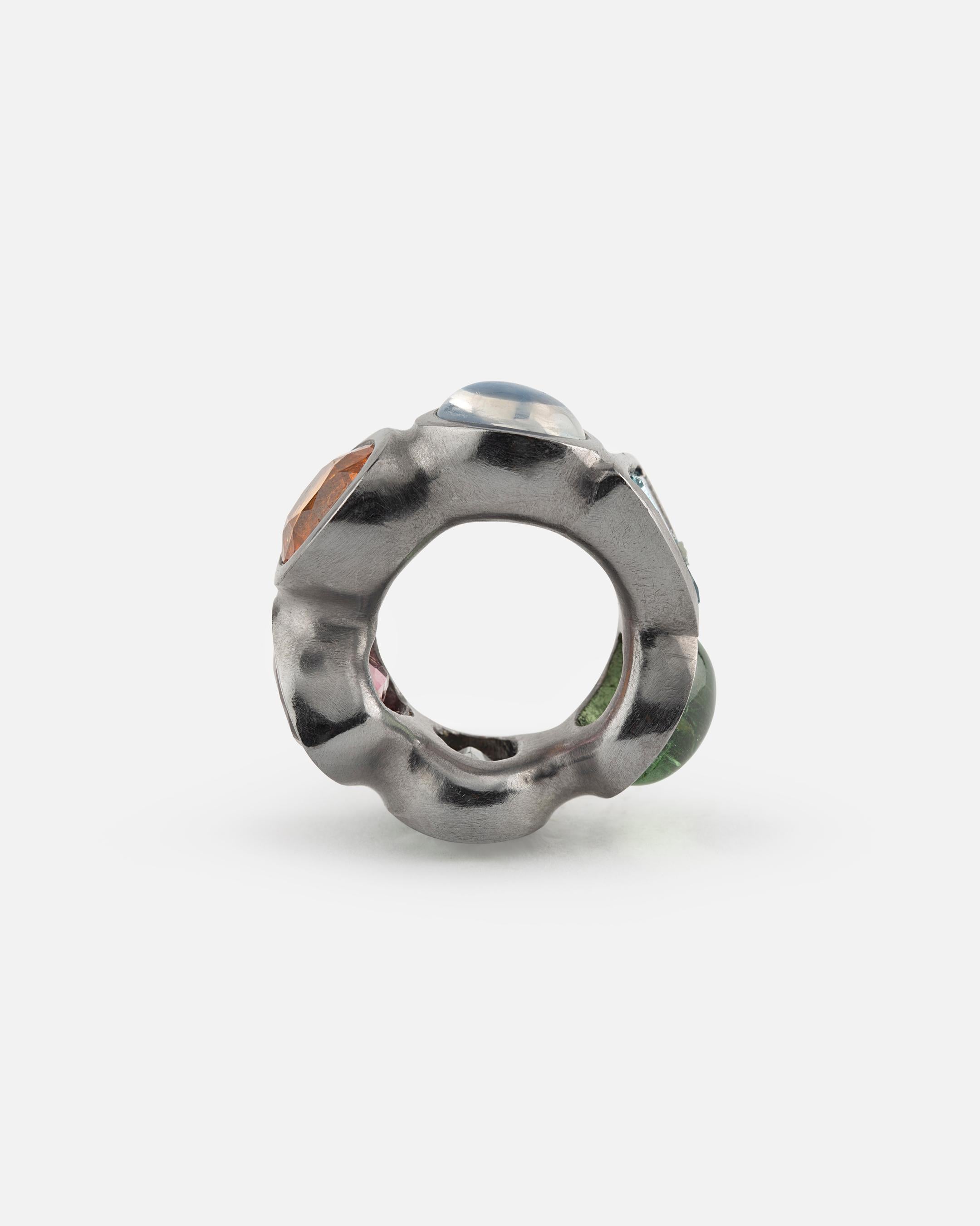 This tantalum ring is carved from one piece. The 6 big gems are pink tourmaline, white topaz, green tourmaline, aquamarine, mandarine garnet (hessonite) and moonstone. Handmade by jewelry-artist Peter Hassenpflug. 
Tantalum is a little-known