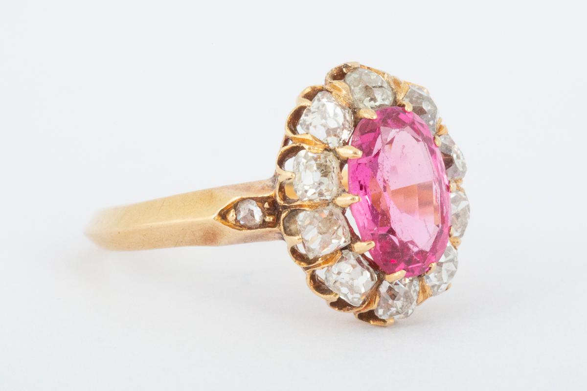 
Oval cluster ring dating from the mid Victorian period. The cluster comprises a large central pink spinel or topaz with a ten stone cushion cut diamond surround. Mounted in 18 carat yellow gold with rose diamond shoulders. The stone weighs