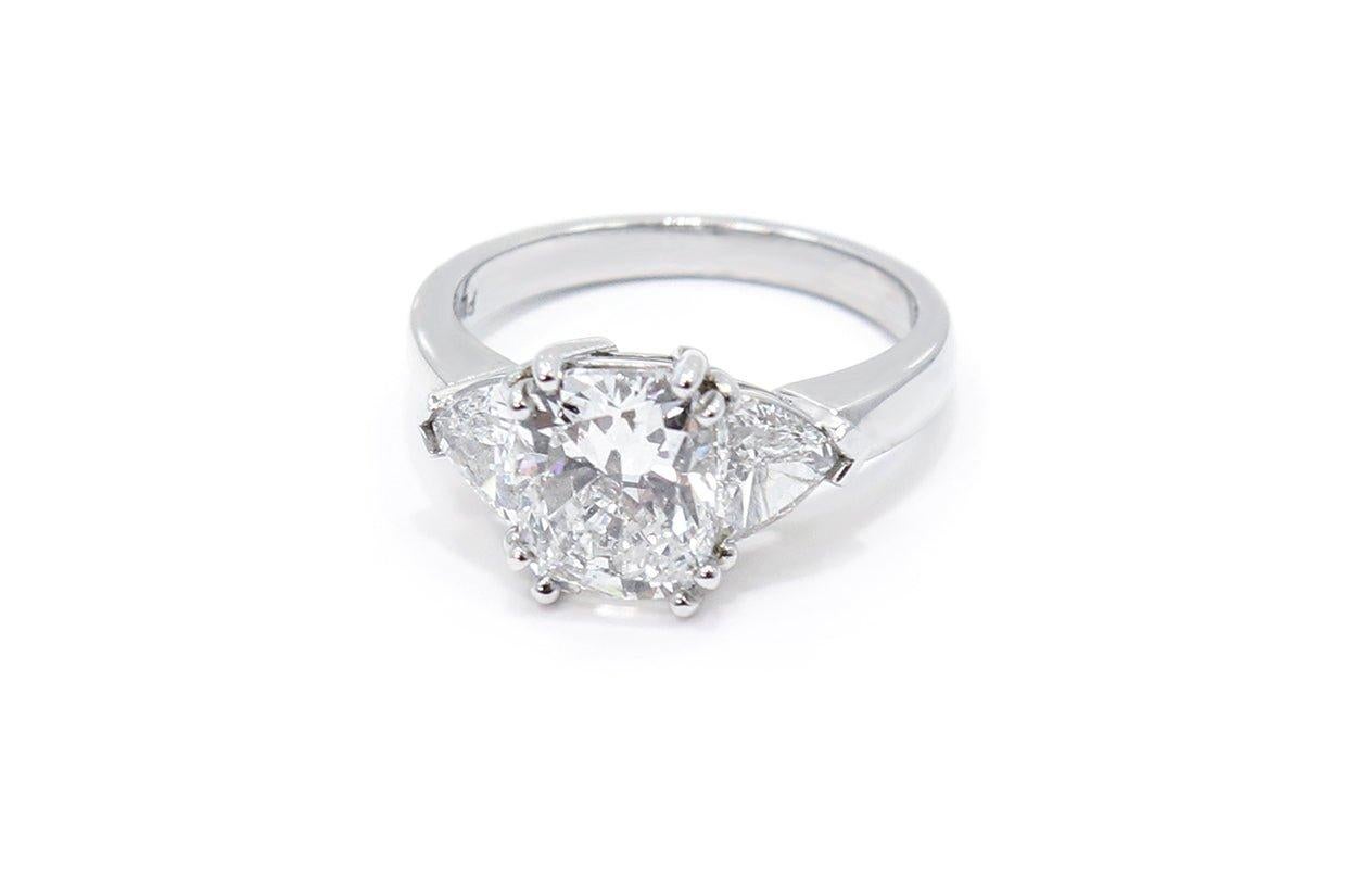 A masterpiece of elegance and sophistication, this platinum three-stone engagement ring showcases a trio of enchanting cushion-cut diamond, each symbol of past, present and future love. Flanked by two exquisite trillion-cut diamonds on either side,