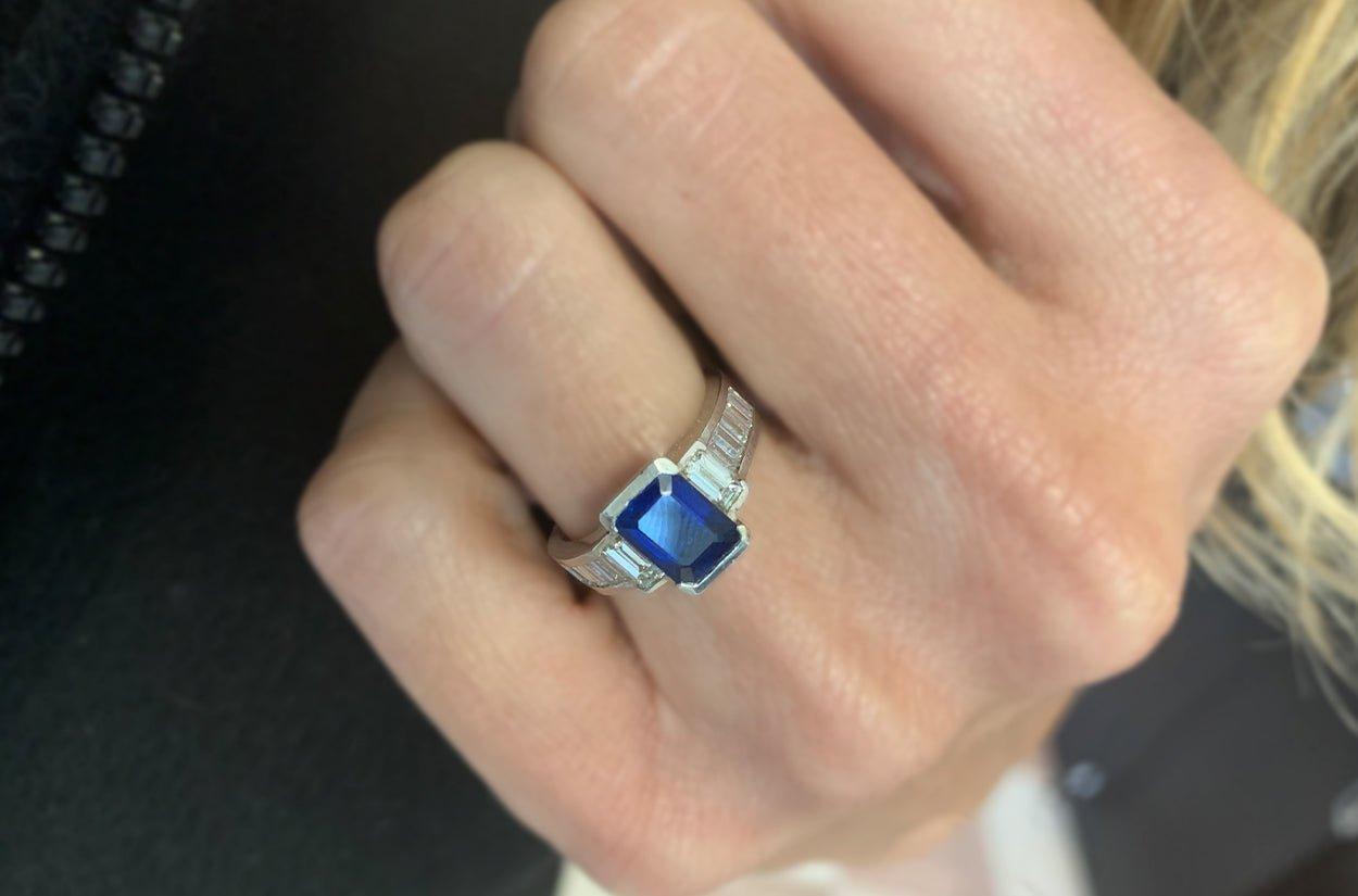 An exquisite Platinum ring featuring a 1.50-carat emerald-cut sapphire, radiating deep, vibrant elegance. Framed by 0.80 carats of dazzling baguette diamonds, this timeless piece offers refined sophistication in a delicate size 5 setting.