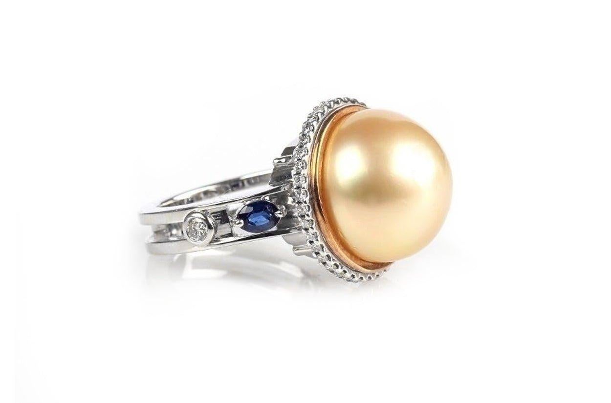 Resplendent 18kt white gold ring, showcasing the luminescence of a golden South Sea pearl at its heart. This radiant pearl is cradled by a brilliant constellation of diamonds, their facets shimmering like stars in the night sky. Graceful oval