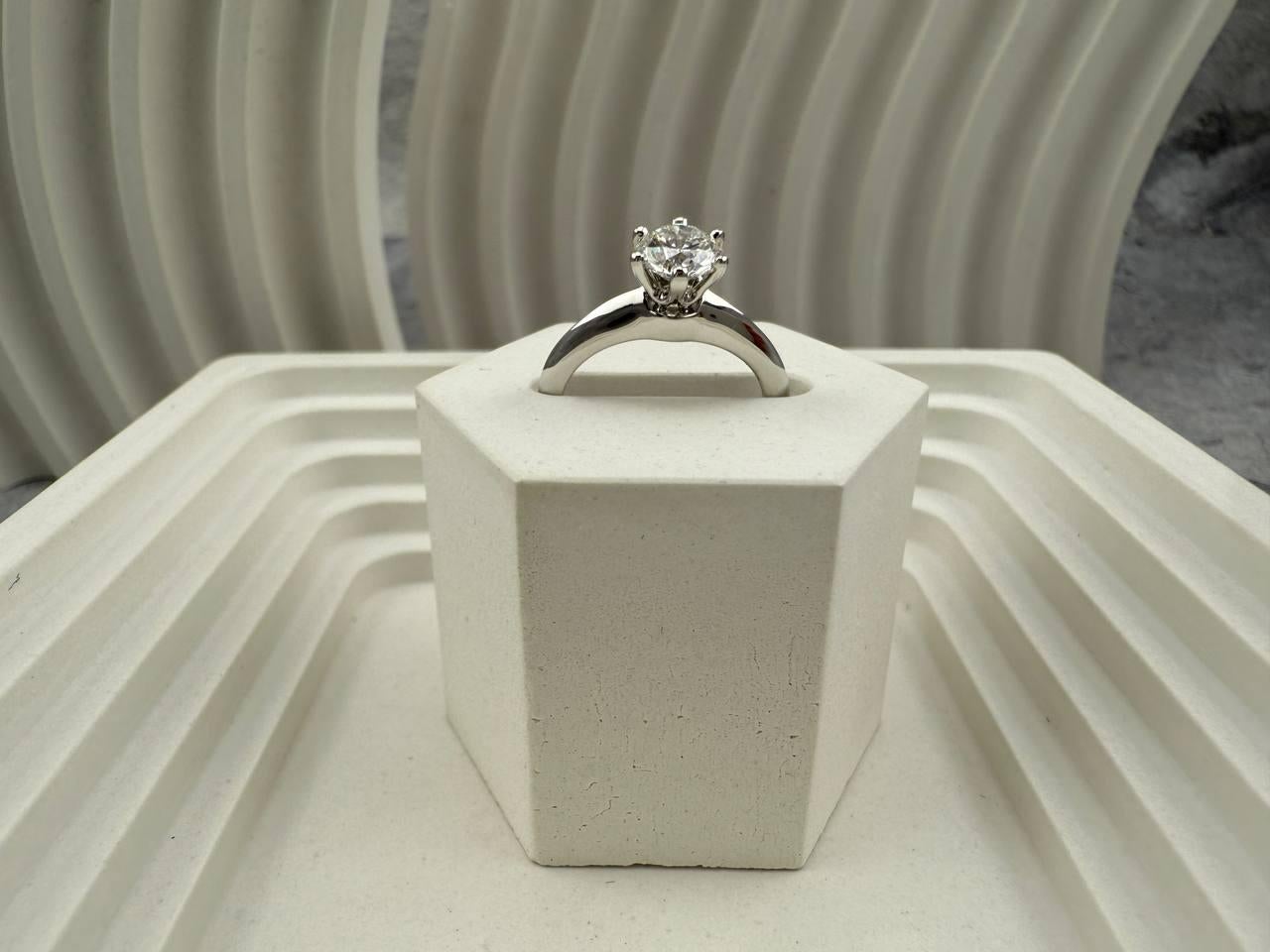 Questo squisito anello di Tiffany & Co. è realizzato in platino 950, a dimostrazione dell'impegno del marchio per un'eleganza senza tempo e una maestria superiore. Al centro c'è un classico diamante rotondo taglio brillante (Cr-57) del peso di 0,62