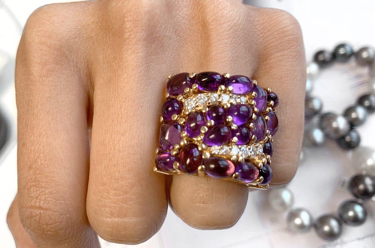 A cluster-style ring, resplendent in 18kt yellow gold, features a captivating arrangement of amethyst cabochons, with their smooth rounded surfaces, radiate a deep and enchanting purple hue, while the diamonds, with their brilliant facets, and a