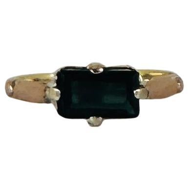 A stunning vintage ring featuring a natural tourmaline gemstone. At first glance, the stone appears black, but when caught by the light, it reveals a deep, captivating dark green hue. The faceted tourmaline is elegantly set in a stunning blend of