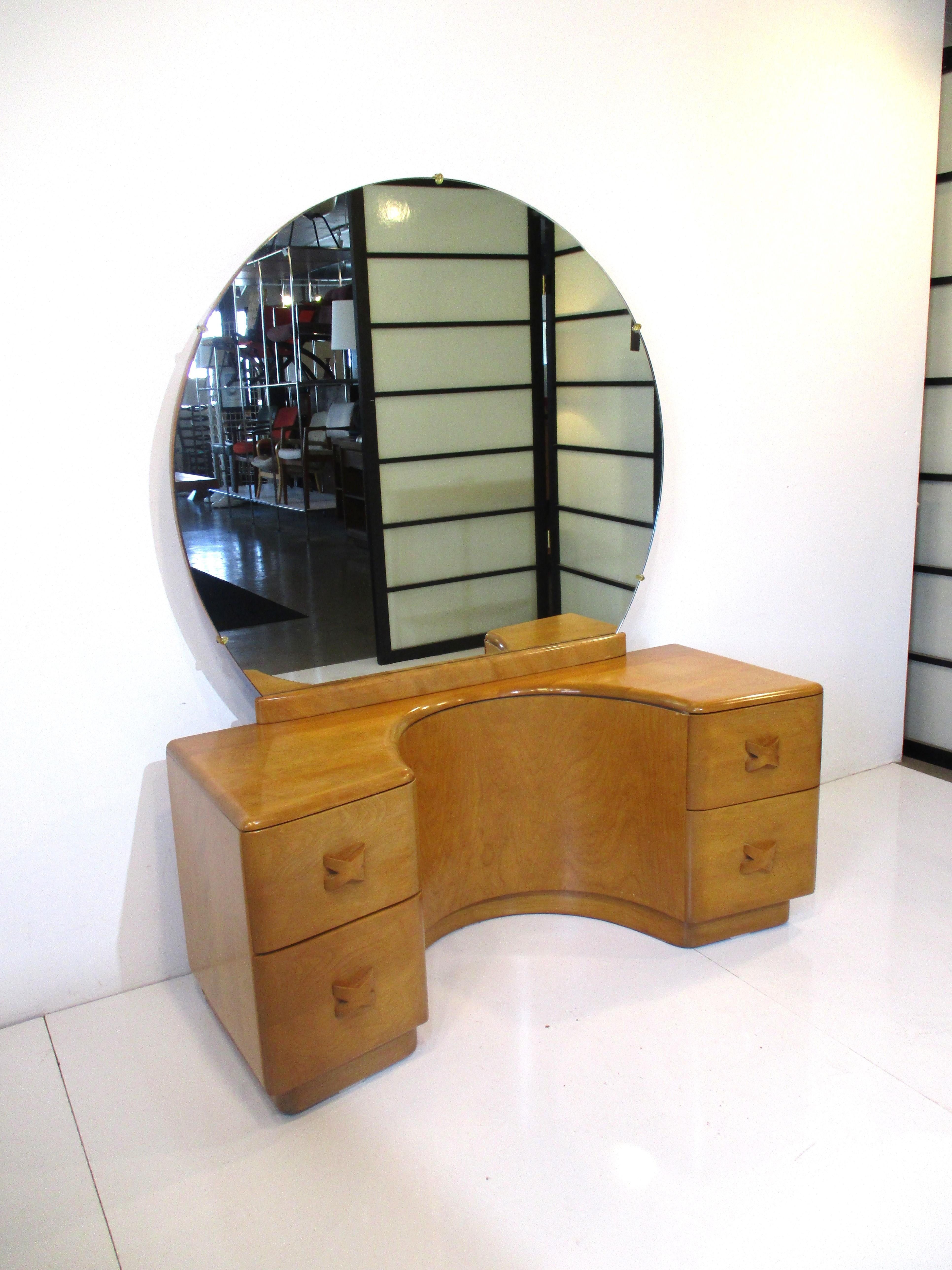 A very well crafted solid maple wood vanity with round mirror sculptural top surface with cut out. The lower area has four drawers with X shaped wooden pulls and it still retains the original stool with original upholstery. Manufactured by the