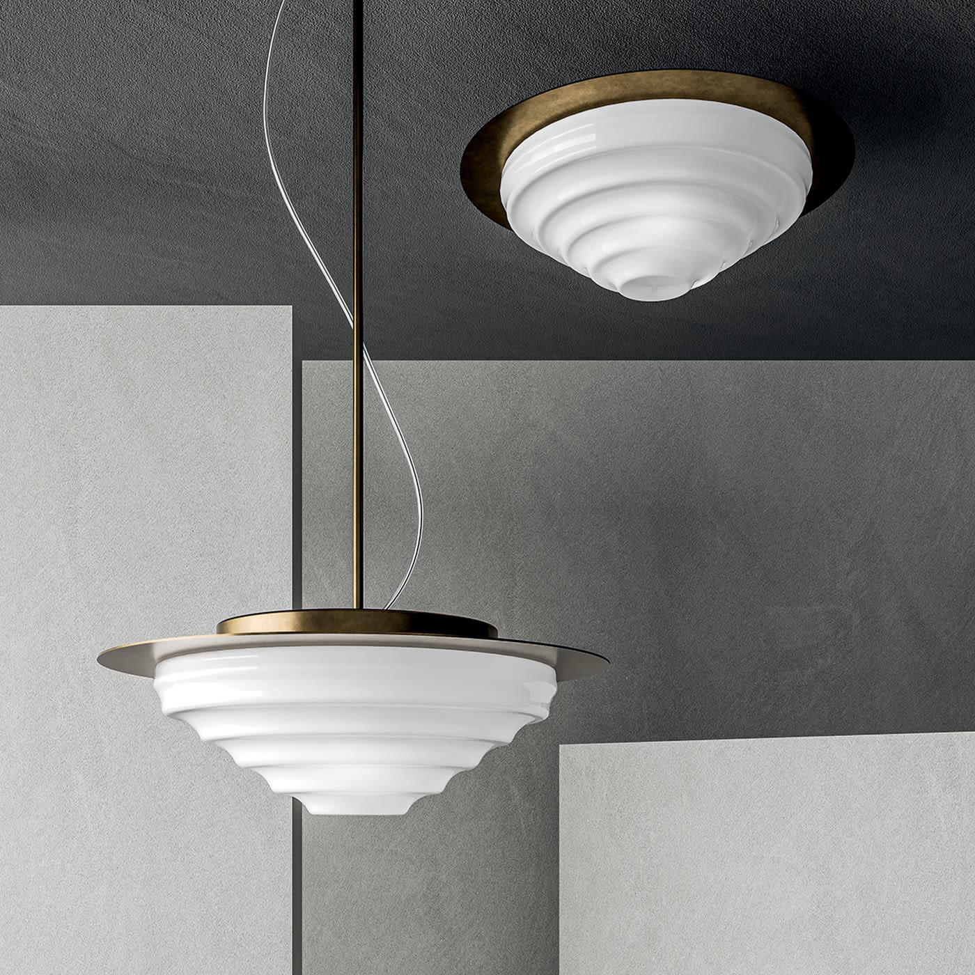 Concentric ripples recalling the water's surface distinguish this marvelous pendant lamp. Offered in a refined burnished finish, the metal structure combines a metal rod with a round plate against which the glossy white Murano glass shade stands.