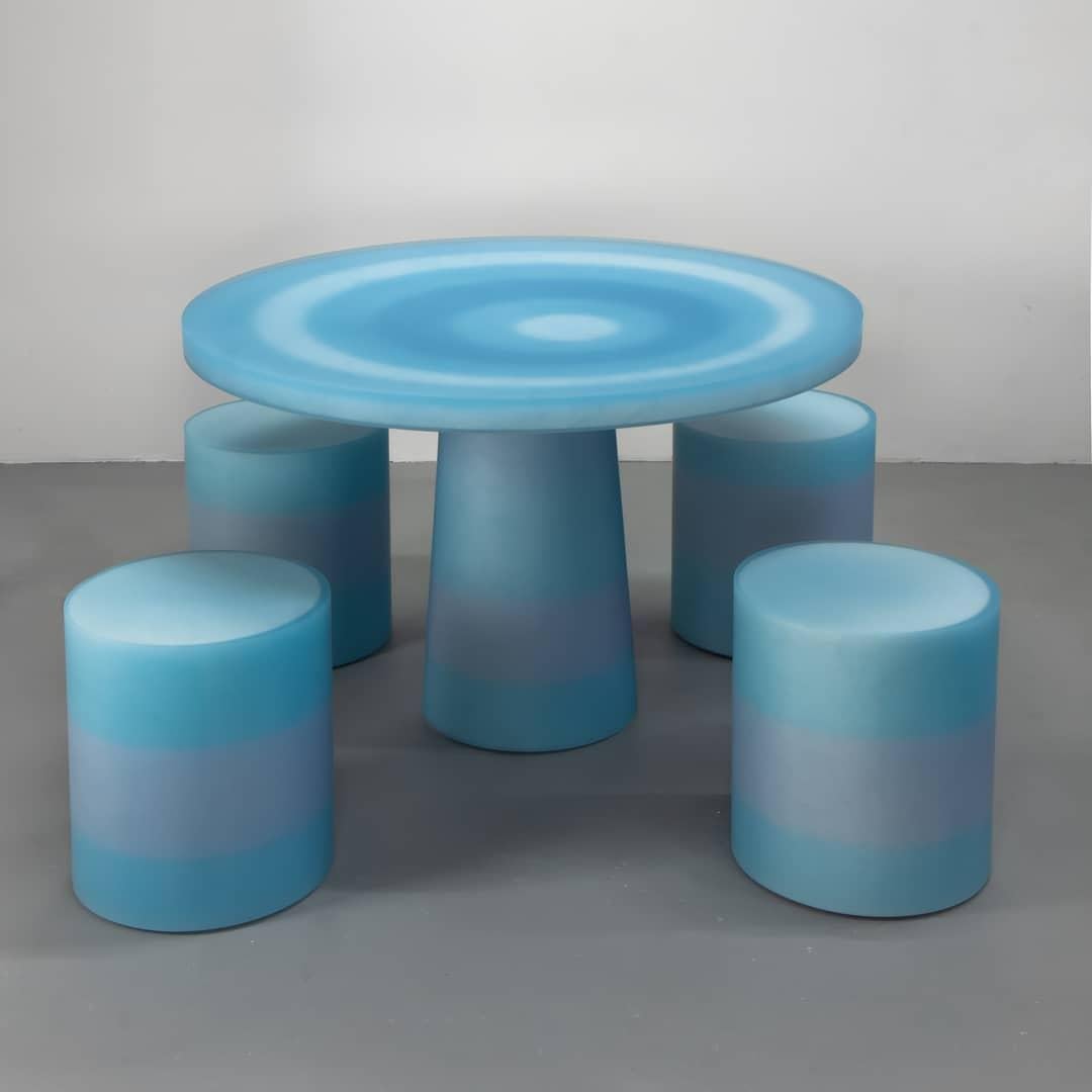 The Ripple resin dining table by Facture Studio consists of a circular top set on a tapered conical base. Simple in design but maximalist in approach, it features a ripple-textured core overlaid with a gradient of colors in a reinterpreted