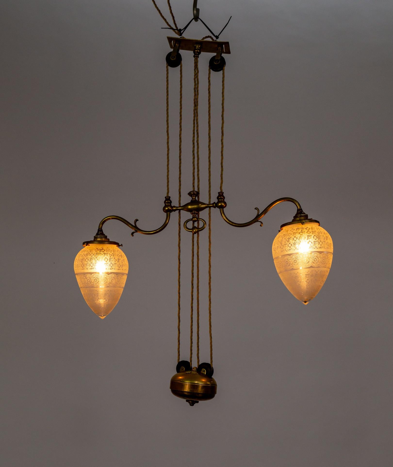 A circa 1900 Rise and Fall ceiling light fixture with textured, beautifully etched torpedo-shaped glass shades. An elegant brass, 2-arm design. The motif has floral and mandala banding and lights with lovely diffusion. The height can be adjusted