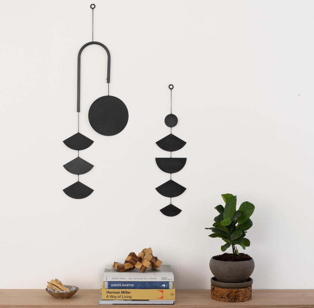 The Rise wall hanging is a modern statement piece that explores the division of a circle. The curved bar adds movement between the counterbalanced components and the striking black patina finish adds a layer of depth to this asymmetrical piece.