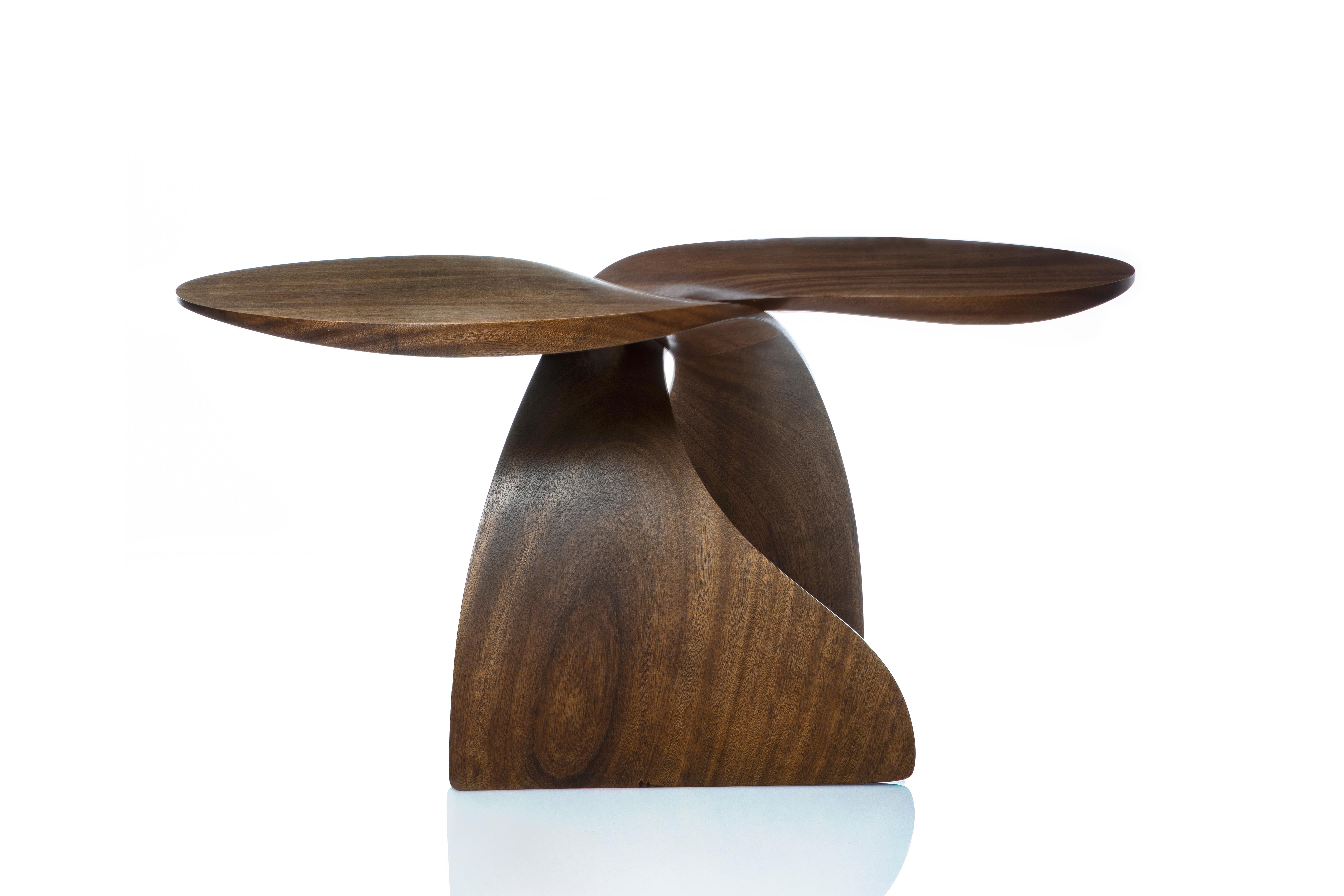 This contemporary table combines the clearly organic shape of the hand carved sweeping base elements, with the contemporary, geometric shape of the tops. Made up of two of identical sapele wood carvings, it has a playful rhythm like a pair of fish,