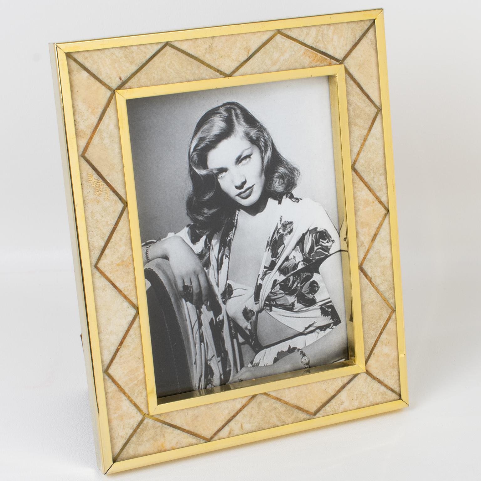 A charming gilded brass and stone picture photo frame designed by Italian designer Rita Frascione, Firenze, in the 1980s. 
The piece features gilded metal framing with marquetry made of brass inlaid and travertine stone in warm beige and gold
