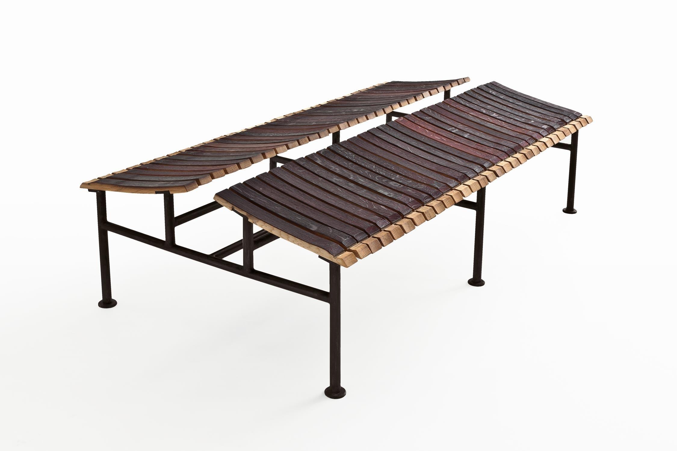 The Chinese Roof Bench, designed by Aldo Cibic for Riva 1920, features a double slanted seat crafted from reclaimed Barrique wood slats, paired with a sturdy iron frame. The bench combines the warmth and character of aged wood with the modern