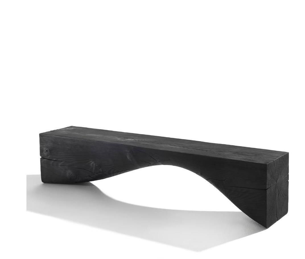 Designer Brodie Neill skillfully combines straight lines and graceful curves in this contemporary bench, showcasing a harmonious blend. Crafted from cedar and available in a rich volcano-black finish, the bench boasts a sophisticated sculptural