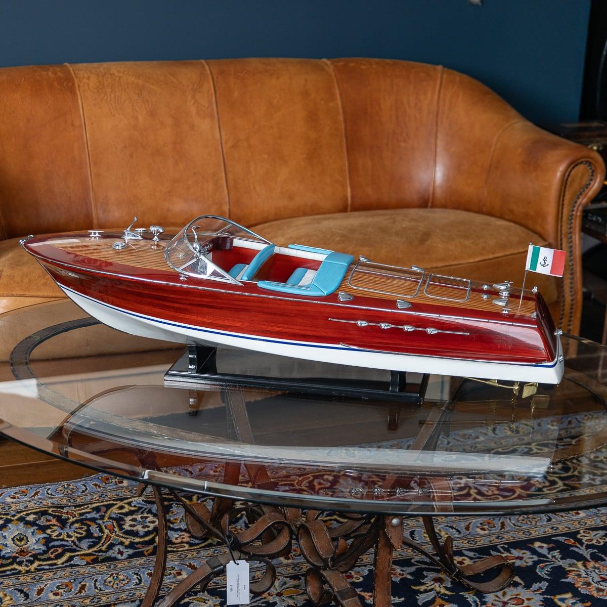 Modèle réduit d'une vedette Riva Triton. Fabriqué à partir de bois fin, de cuir souple et de détails chromés. Il présente une finition bicolore avec du bois laqué naturel et du blanc sous la ligne de flottaison. Le savoir-faire artisanal est évident