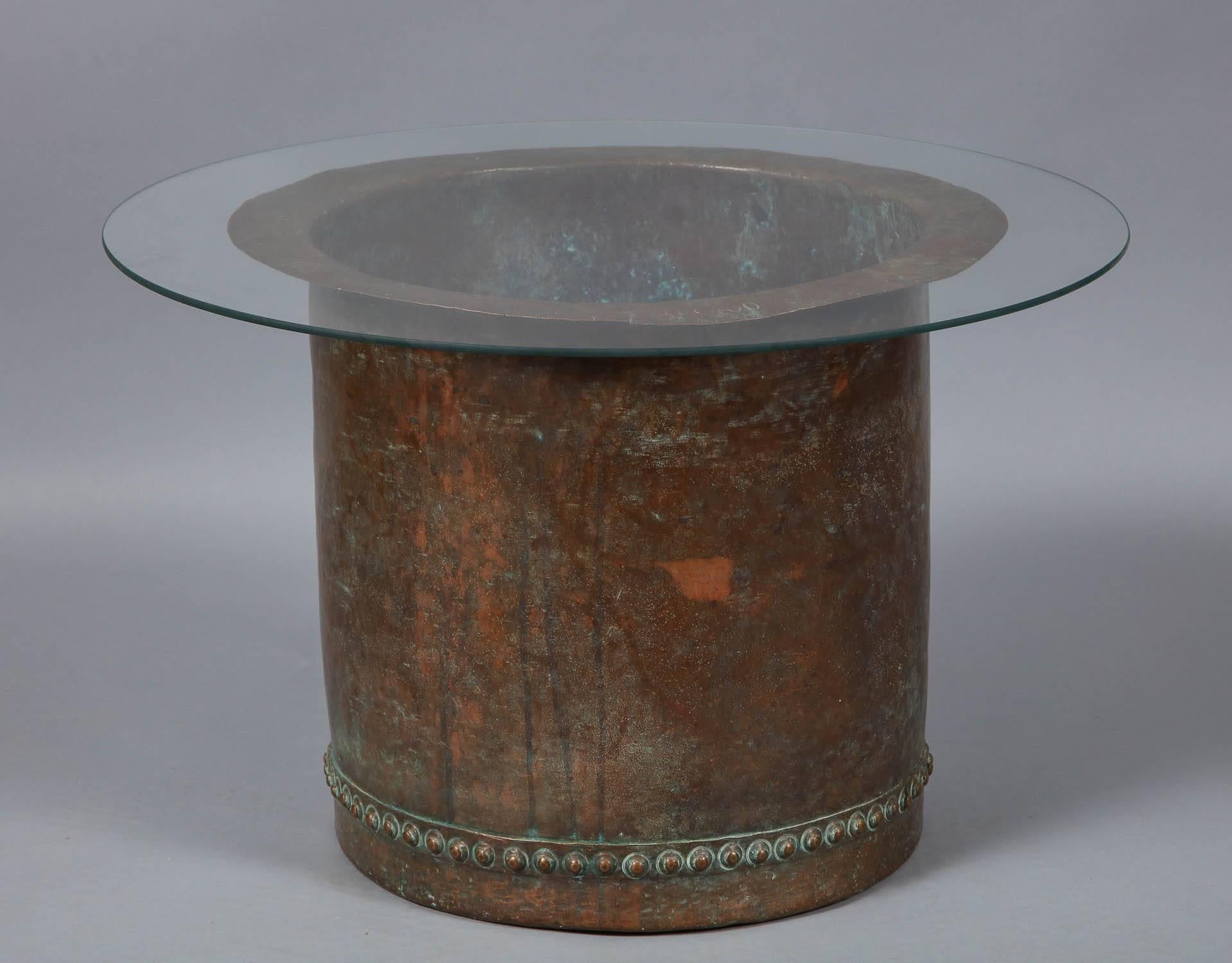 A fantastic riveted copper oversize log bin having beautiful bronzed patina, and top-hat form, as coffee table with glass top. Measure: 18