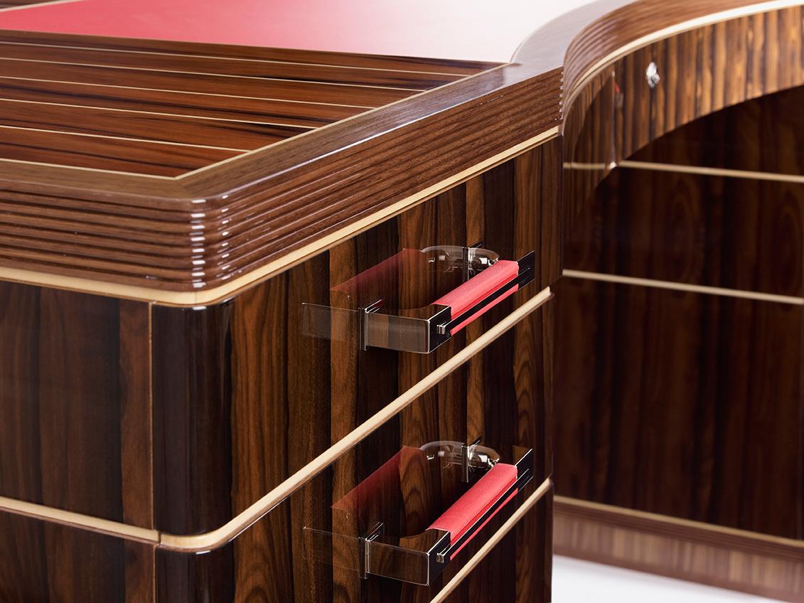 The Linley Riviera rouge desk is a unique desk with a high gloss finish featuring a Santos rosewood top and inlaid sycamore pinstripe inspired by yacht decking. The sides and front are constructed with inlaid Ziricote, complemented by nickel handles