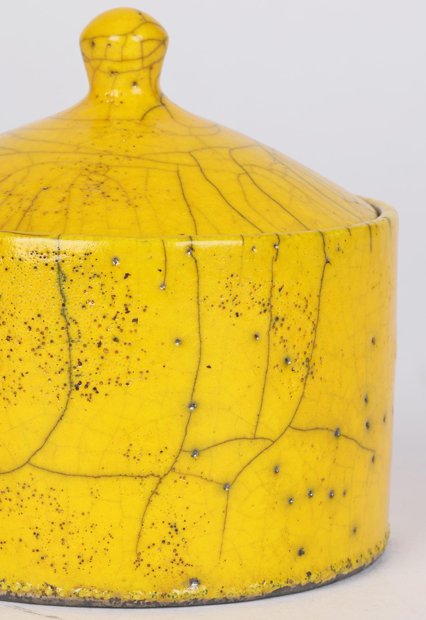 A very finely made British studio pottery lidded pot decorated with yellow raku fired glazes by Rob Hand (British, b.1948) and dating from the latter 20th or early 21st century. The pot has a round cylindrical shaped body with a flat base with a