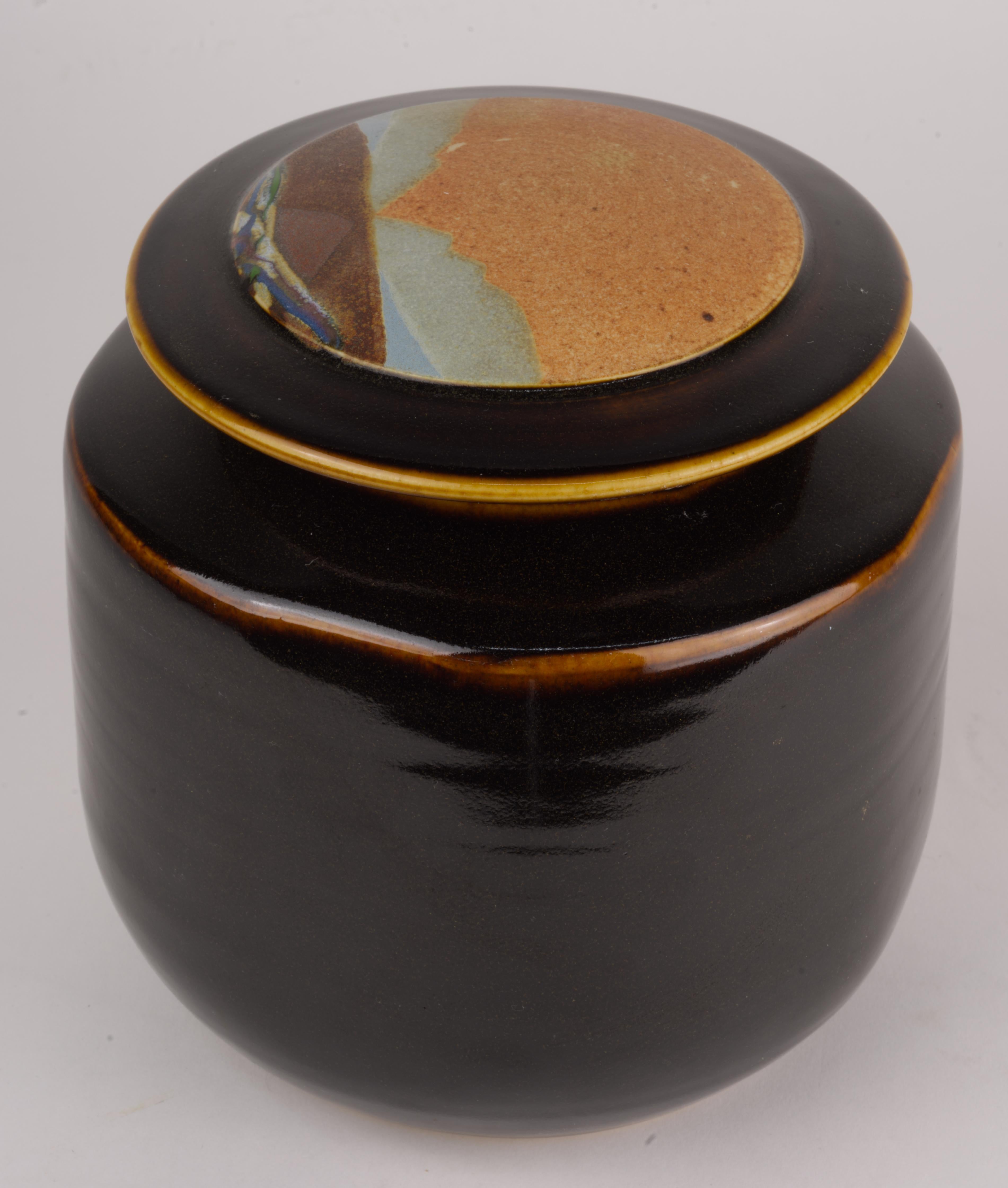  Covered vessel or jar was handmade in white clay by Rob Wiedmaier of River Hills Pottery as a part of a series done in 1980s. The lid of the vessel is decorated with abstract landscape design done in complex mix of multicolored, textured matte and