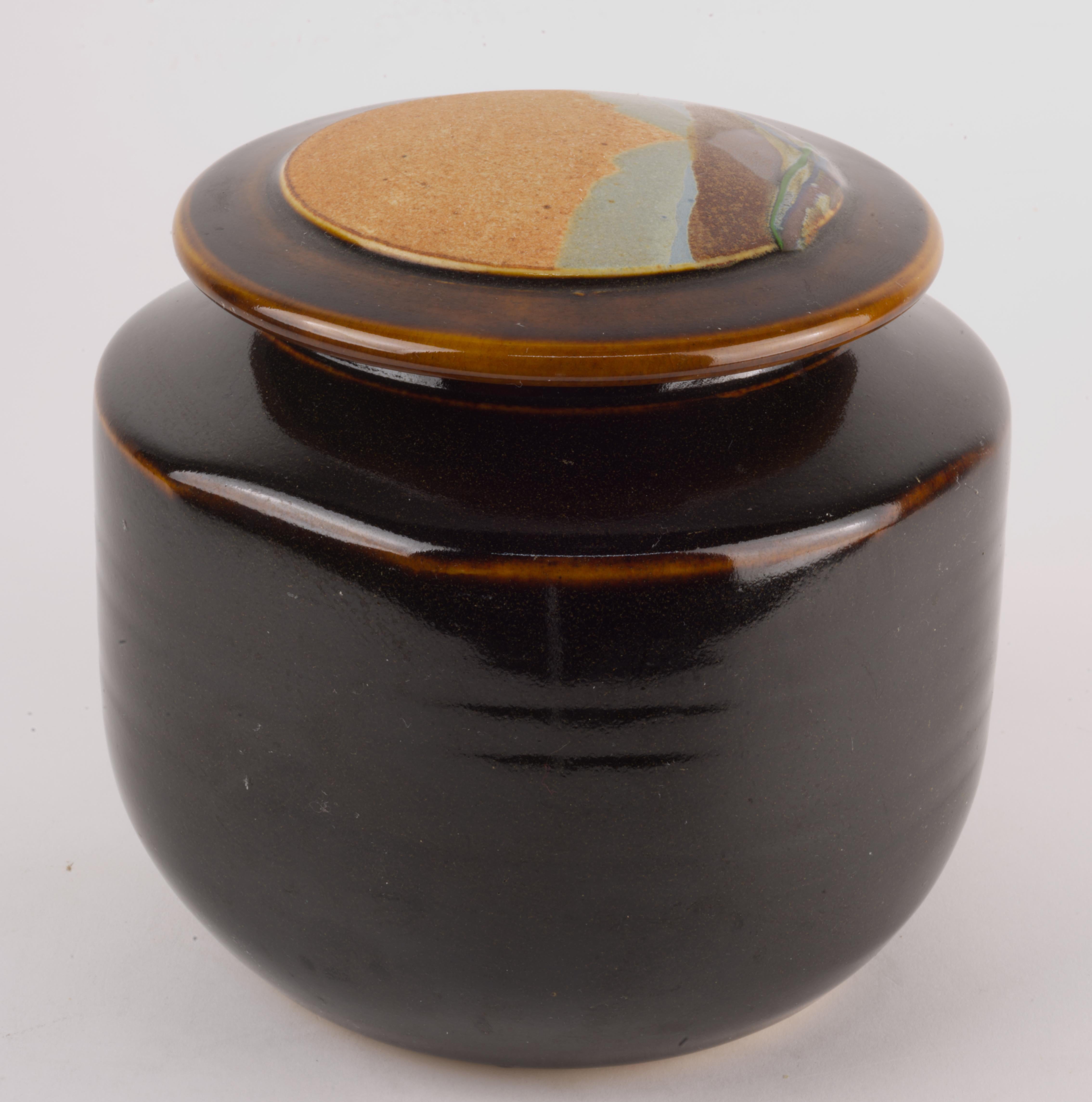  Covered vessel or jar was handmade in white clay by Rob Wiedmaier of River Hills Pottery as a part of a series done in 1980s. The lid of the vessel is decorated with abstract landscape design done in complex mix of multicolored, textured matte and