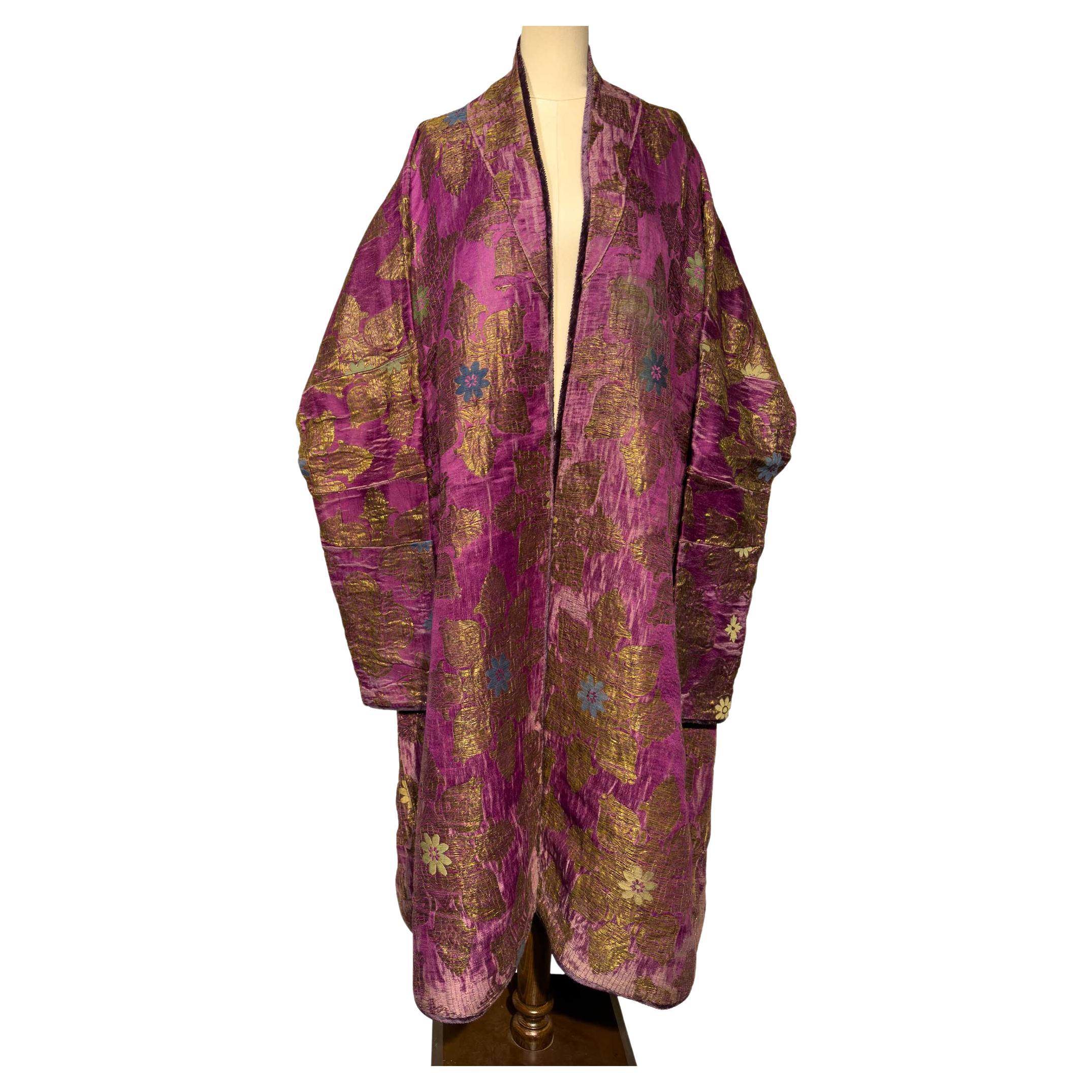 Este abrigo de brocado de seda uzbeko de mediados del siglo XIX se distingue por su luminoso fondo magenta y sus motivos florales dorados a gran escala, acentuados con sutiles toques de azul y marfil. Los brillantes hilos metálicos y la saturada