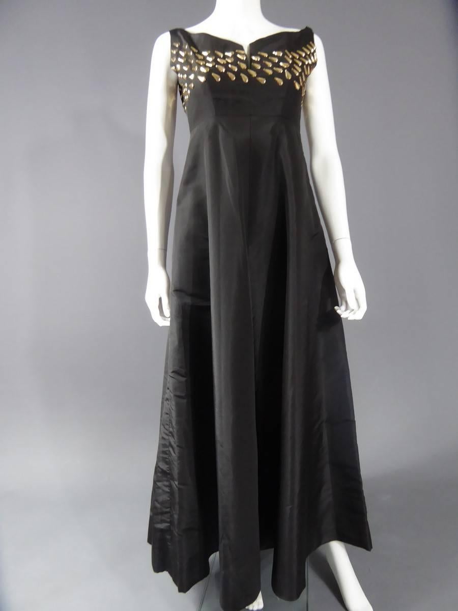 Circa 1960
France
Keats model executed by Maria Carine special permission , the beautiful long evening dress in black silk taffeta, with an effect size haute.Décolté embroidered boat rhodoïd gold pellets. flared skirt ending at the ankle.
Equivalent