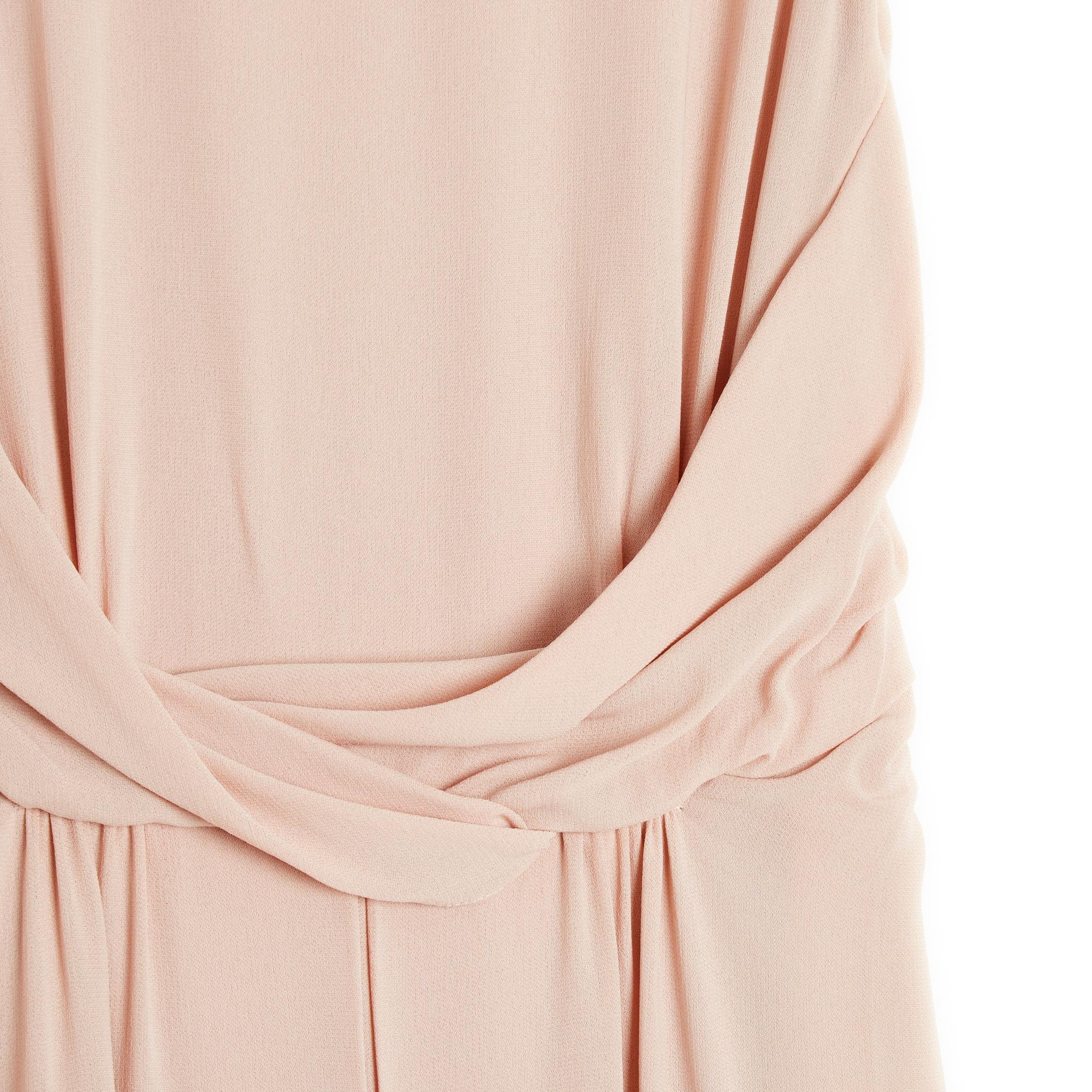 Long dress in pale pink beige silk crepe (flesh or nude), sleeveless, draped at the waist, long straight skirt with wide hollow pleat in front, V-neckline in the back draped on each side of the long zip closure, decorated with 2 small ties to tie