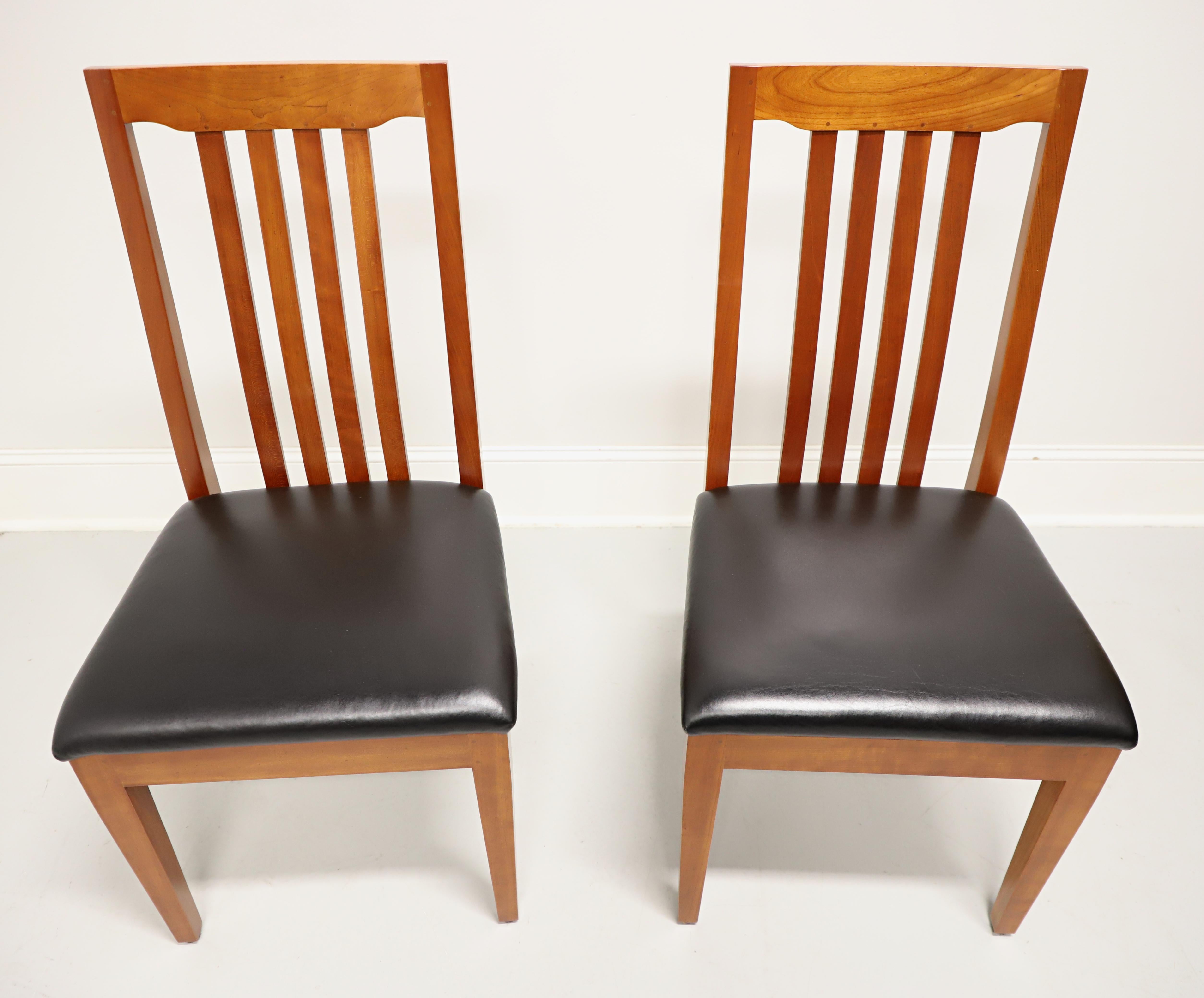 A pair of custom crafted dining side chairs in the Mission style by Robert Bergelin Co, of Morganton, North Carolina, USA. Handmade of cherry wood with open slat backs, black leather upholstered seat, and tapered straight front legs. Made in the