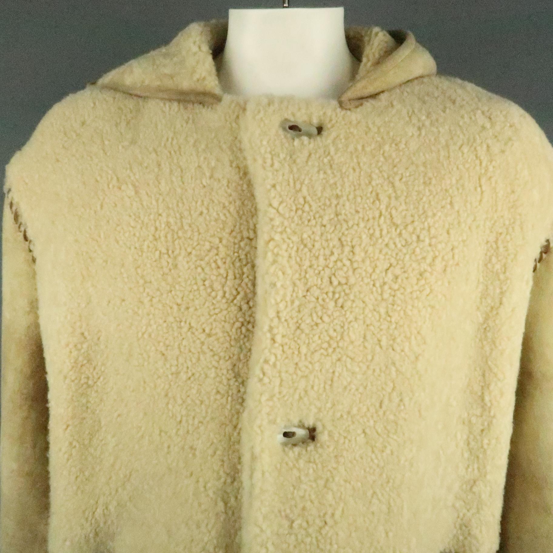 ROBERT COMSTOCK coat comes in a tan sherling featuring a hooded style, leather stitched details, abstract buttons, and patch pockets. Made in Spain.
 
Very Good Pre-Owned Condition.
Marked: (No size)
 
Measurements:
 
Shoulder: 24.5 in.
Chest: 52