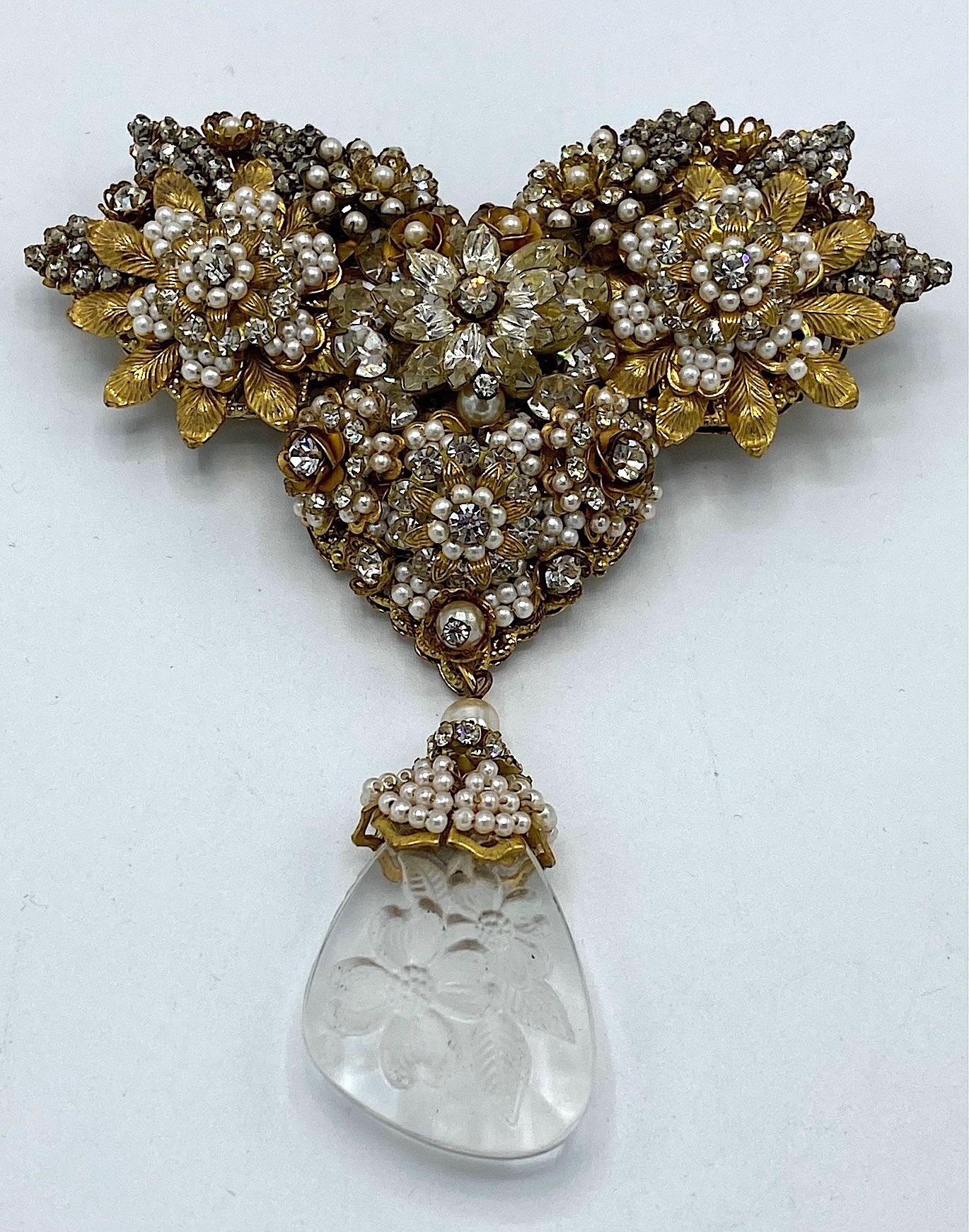 Presented here is a rare and large brooch from the late 1950s to early 1960s by Robert DeMario. The openwork lace like metal is gold plated and wired with faux seed pearls and rhinestones in a floral motif. Hanging from the bottom is a floral etched