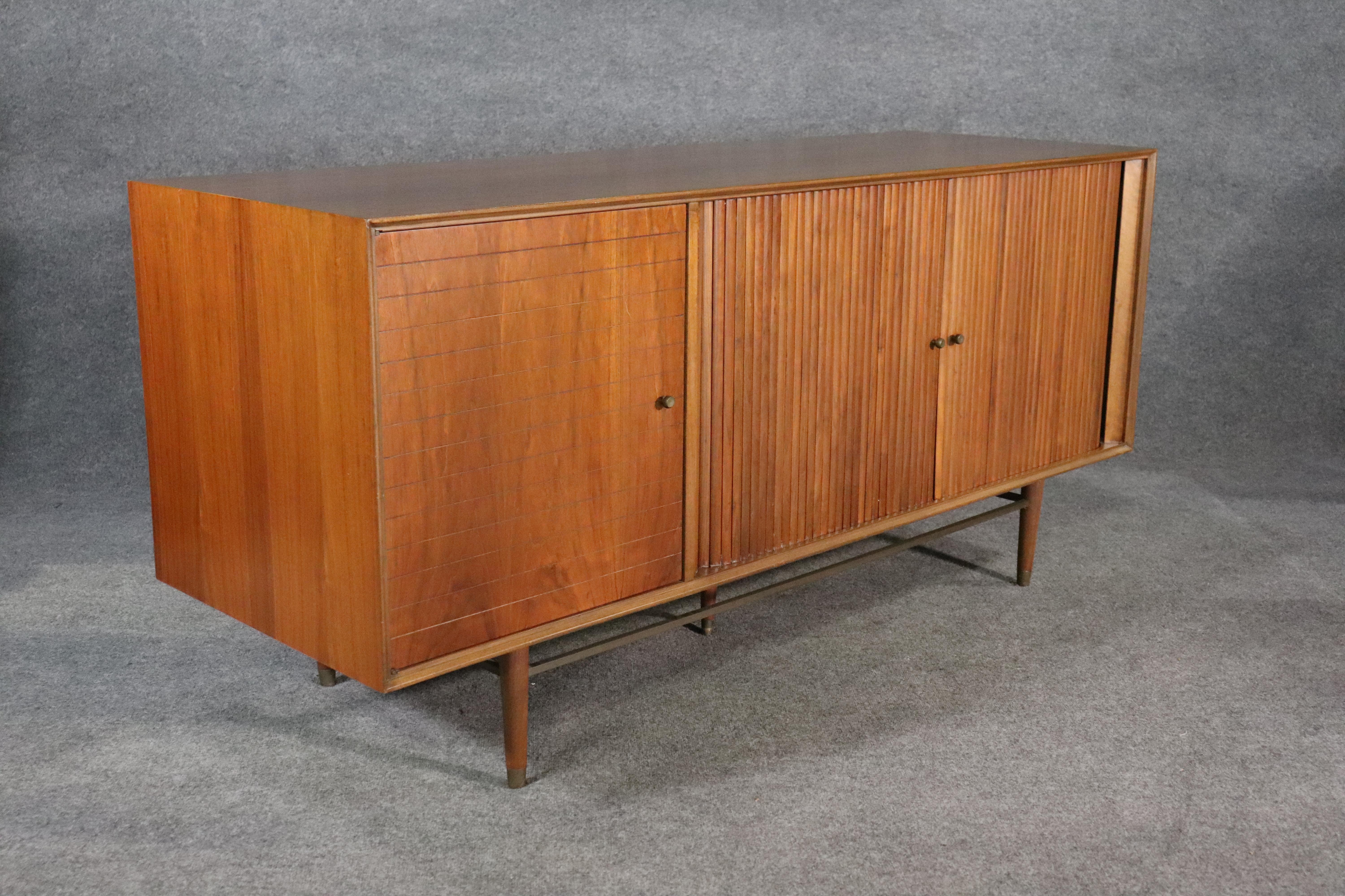 Long mid-century modern credenza with rolling tambour doors, designed by Furst and Fellner for Furnette Inc. Great modern design with walnut grain and accenting brass hardware.
Please confirm location NY or NJ