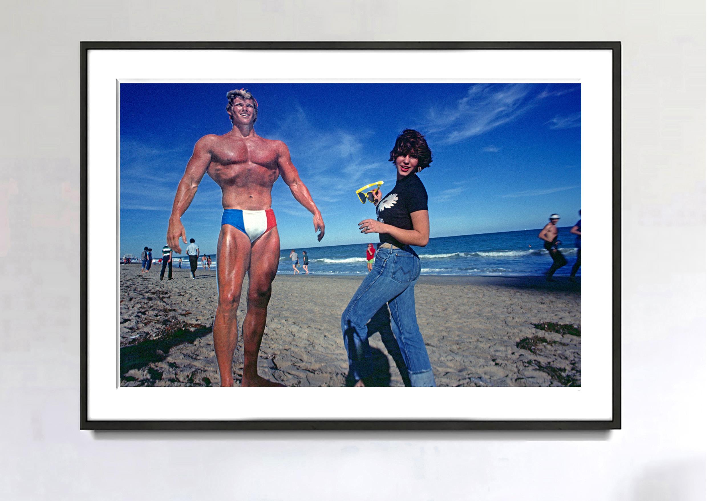 A ripped muscleman strikes the pose with an admiring female bystander who holds an oversized pair of prank sunglasses. In reality, the muscleman is a 5-inch cut-out, and the girl is lifesize. Notice the small cast shadow on the bottom of the