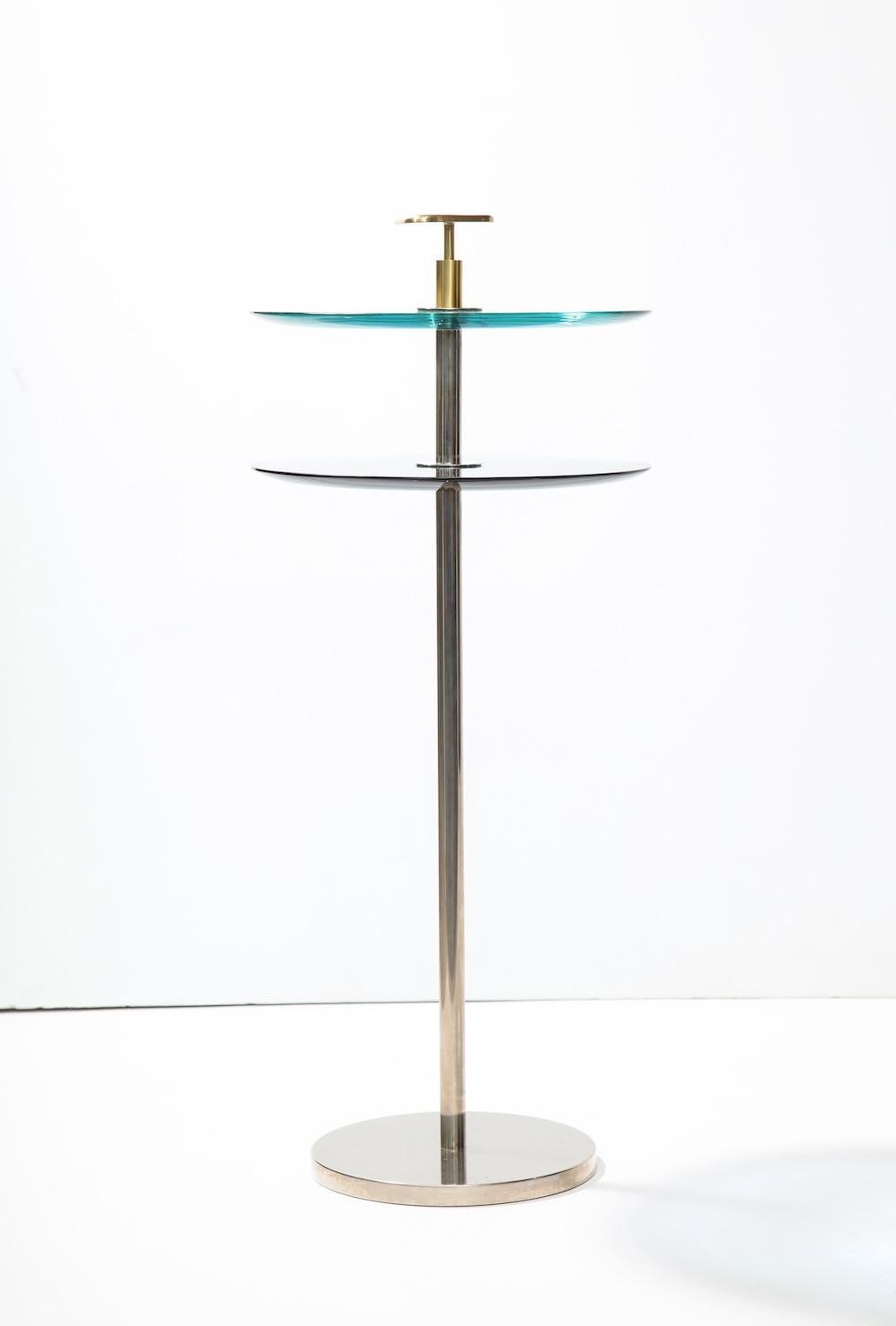 2-tier side table By Robert Giulio Rida. Elegant table with 1 blue glass surface and one clear glass surface. Nickeled brass base and polished brass finial. Signed by artist. 2nd matching tables available.