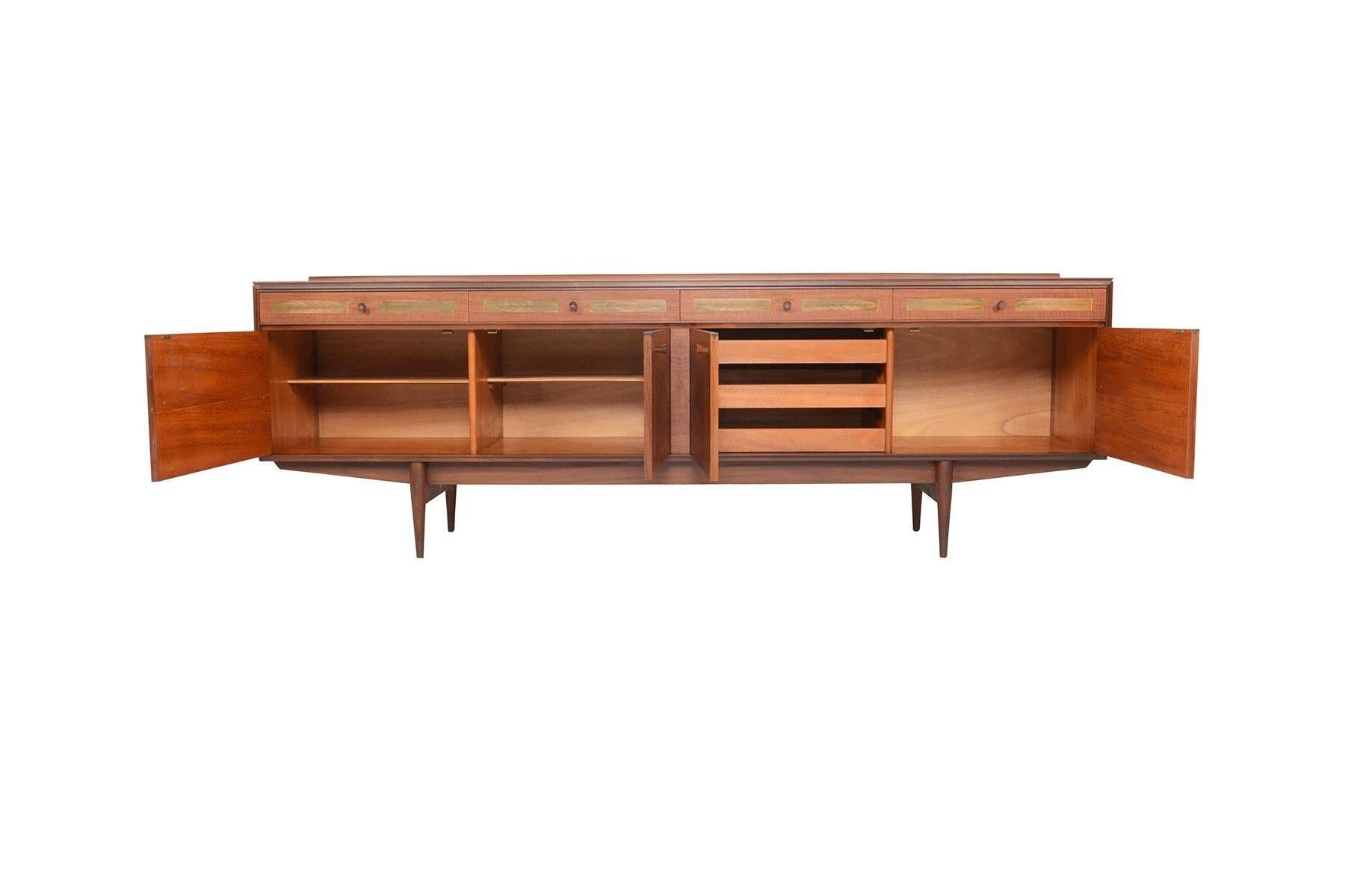 This English modern midcentury large teak credenza was designed by Robert Heritage for Archie Shine Furniture in the 1960s. This stately piece offers four bays outfitted with removable shelves and drawers. Four drawers sit above, each adorned with