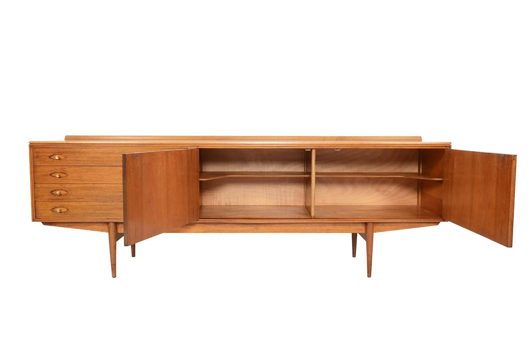 This long English modern credenza was designed by Robert Heritage for Archie Shine Furniture in 1957. Known as the “Hamilton” model, this beautiful piece is cased in mahogany with a curved lip in the back. Two rosewood doors open to reveal two bays