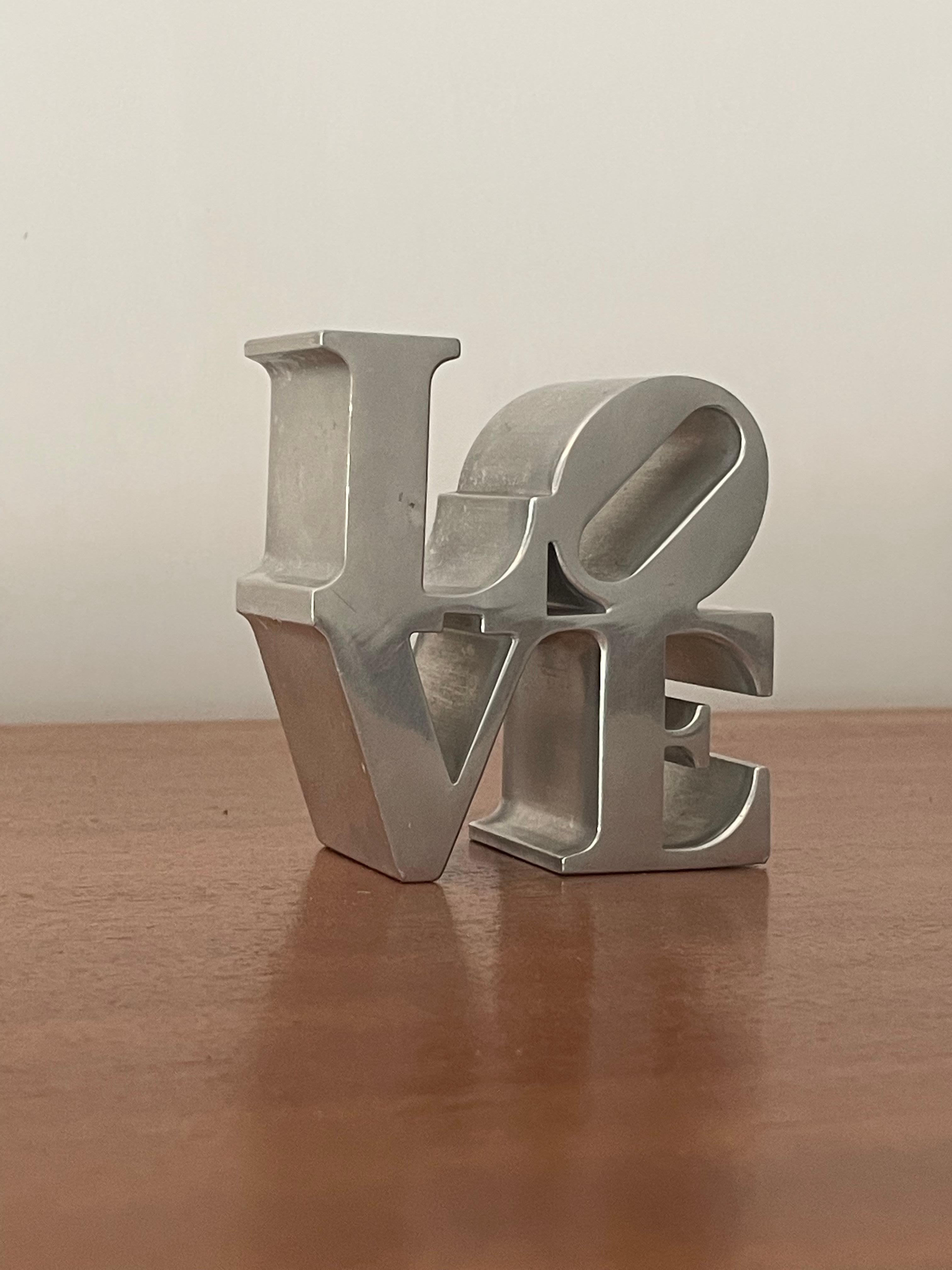 A paperweight in metal after Robert Indiana. Likely purchased at MoMA. This piece would add character to any desk or office environment.