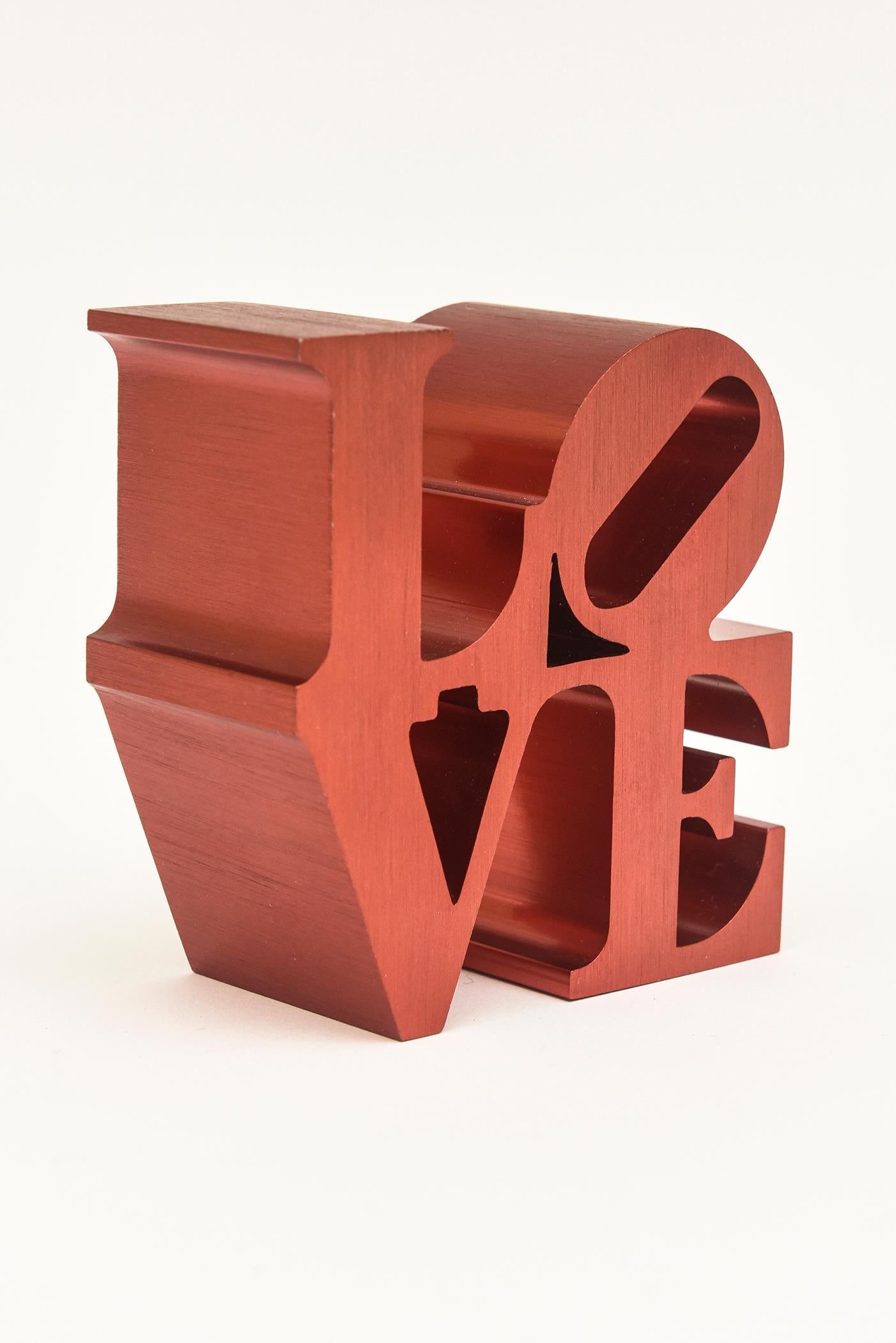 This very rare rendition and small edition of the vintage Robert Indiana love paperweight sculpture is rarely seen version in red brushed aluminum. This may have only been a very small and finite number of these made in the 1970s. We all need more