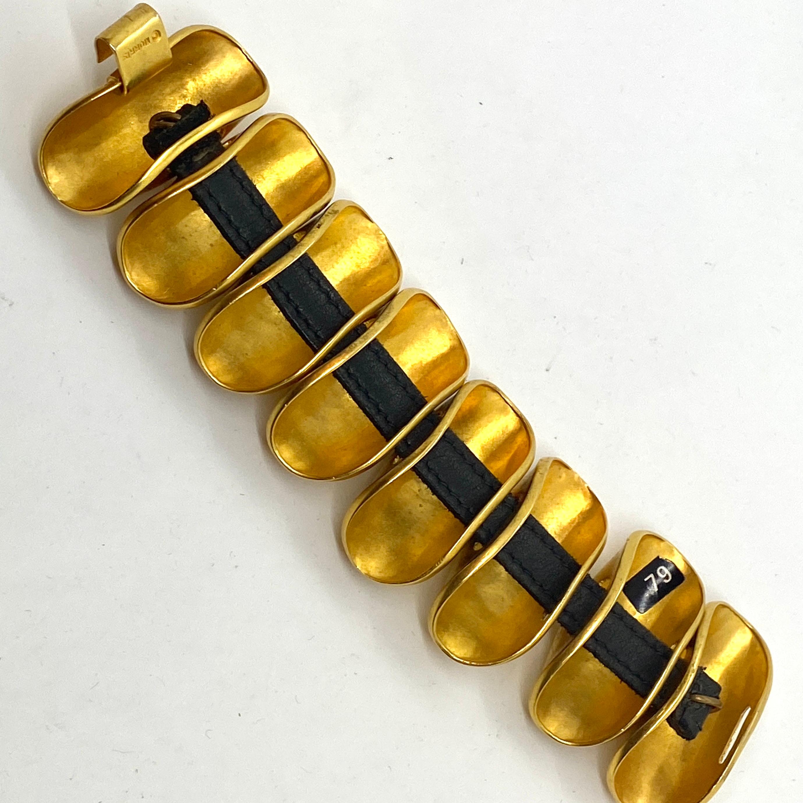 One of the most iconic designs from Robert Lee Morris is this matte gold plated brass bracelet with 8 large knuckle ring slides on a leather strap. the clasp is quite primitive and fits with the gutsy design of this piece. there is spontaneous joy