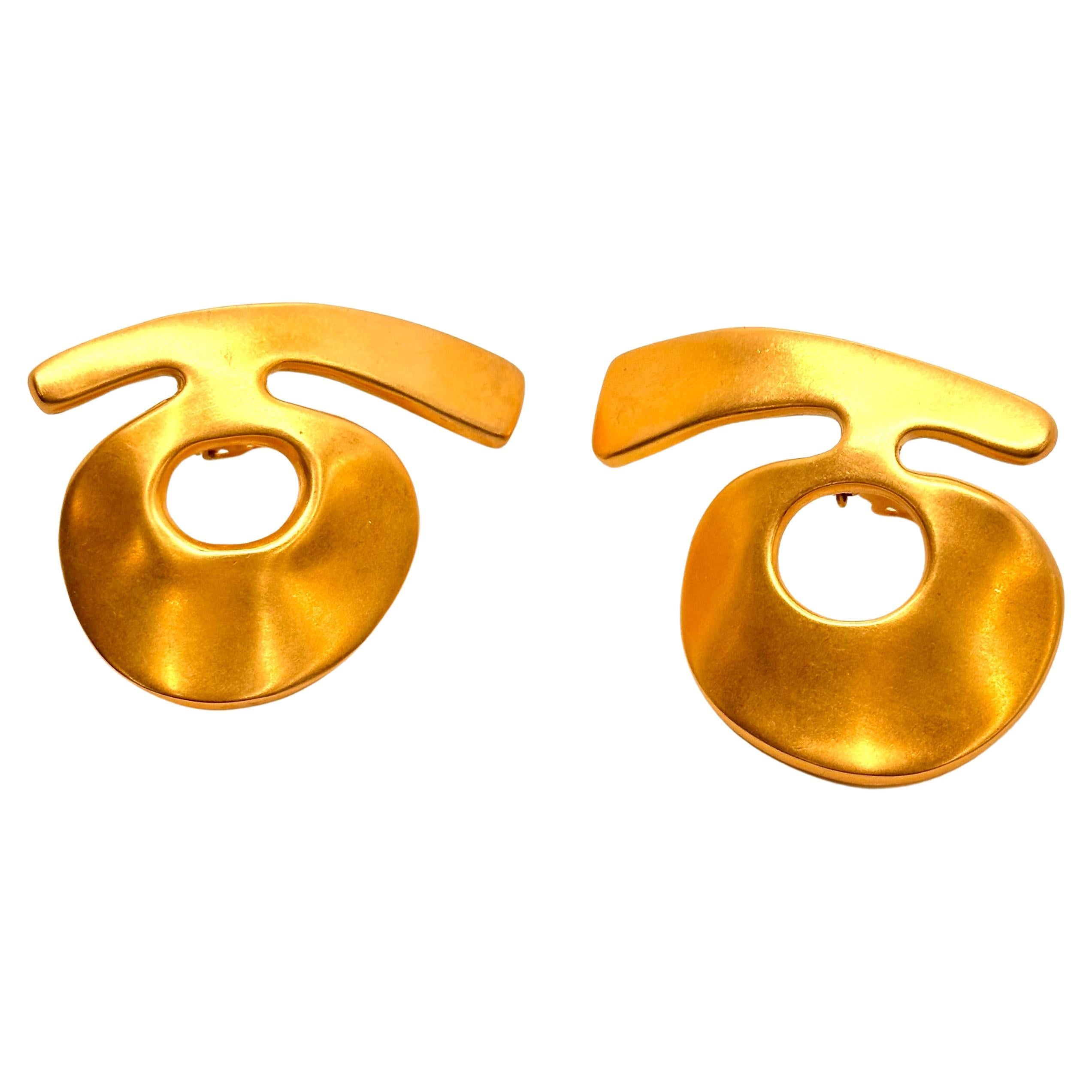 These very unusual Bold /Gold earrings are actually buttons in that they are clips and sit high on the ear. The dynamic design features a curving cross bar over an attached donut form, like some alien calligraphy. Modern and daring, these earrings