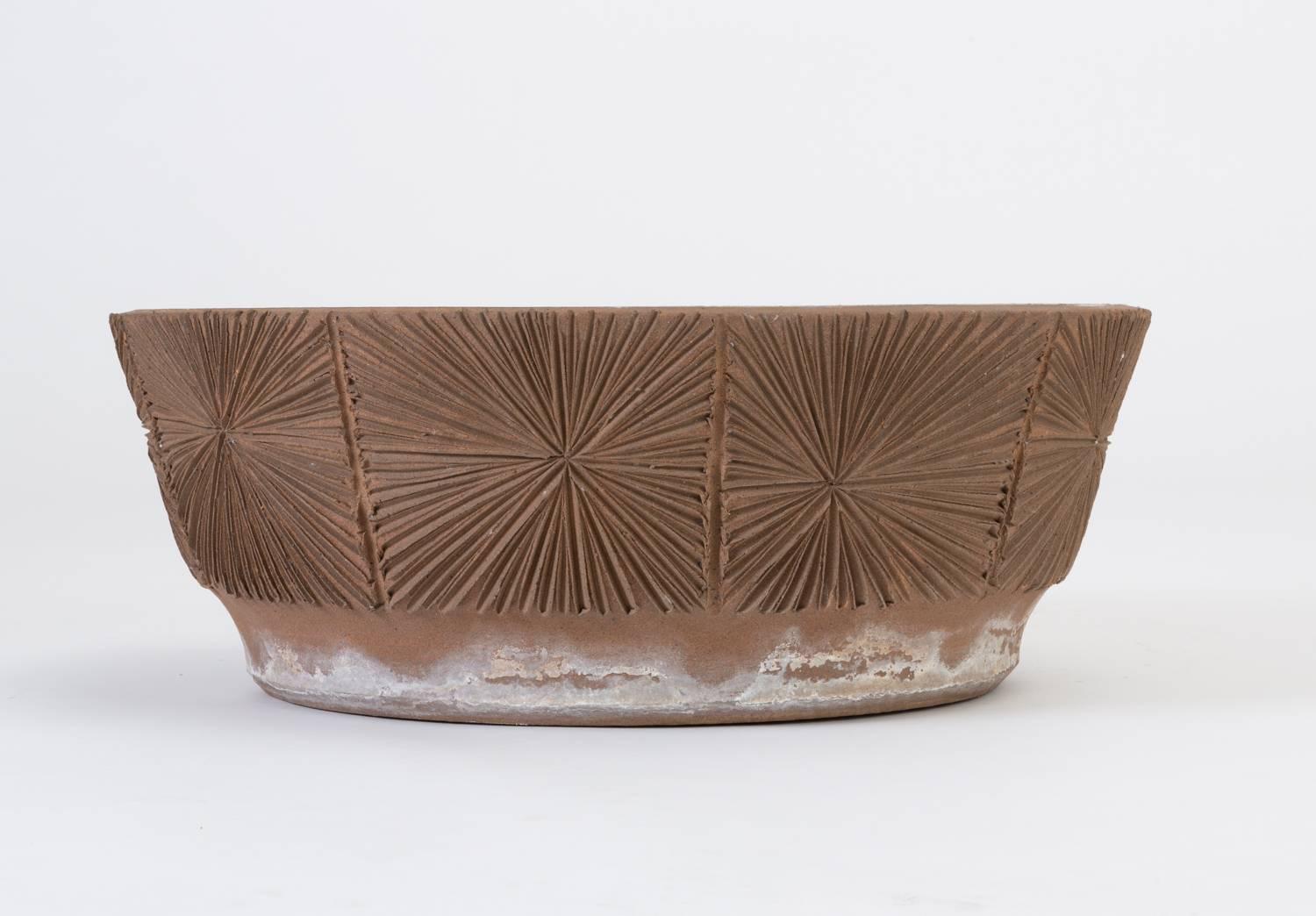 A stoneware saucer planter from David Cressey/Robert Maxwell 1970s collaboration Earthgender. The planter has flat, angled sides and an incised all-over sunburst pattern. Unglazed. 

Condition: Excellent original condition; hard water buildup on