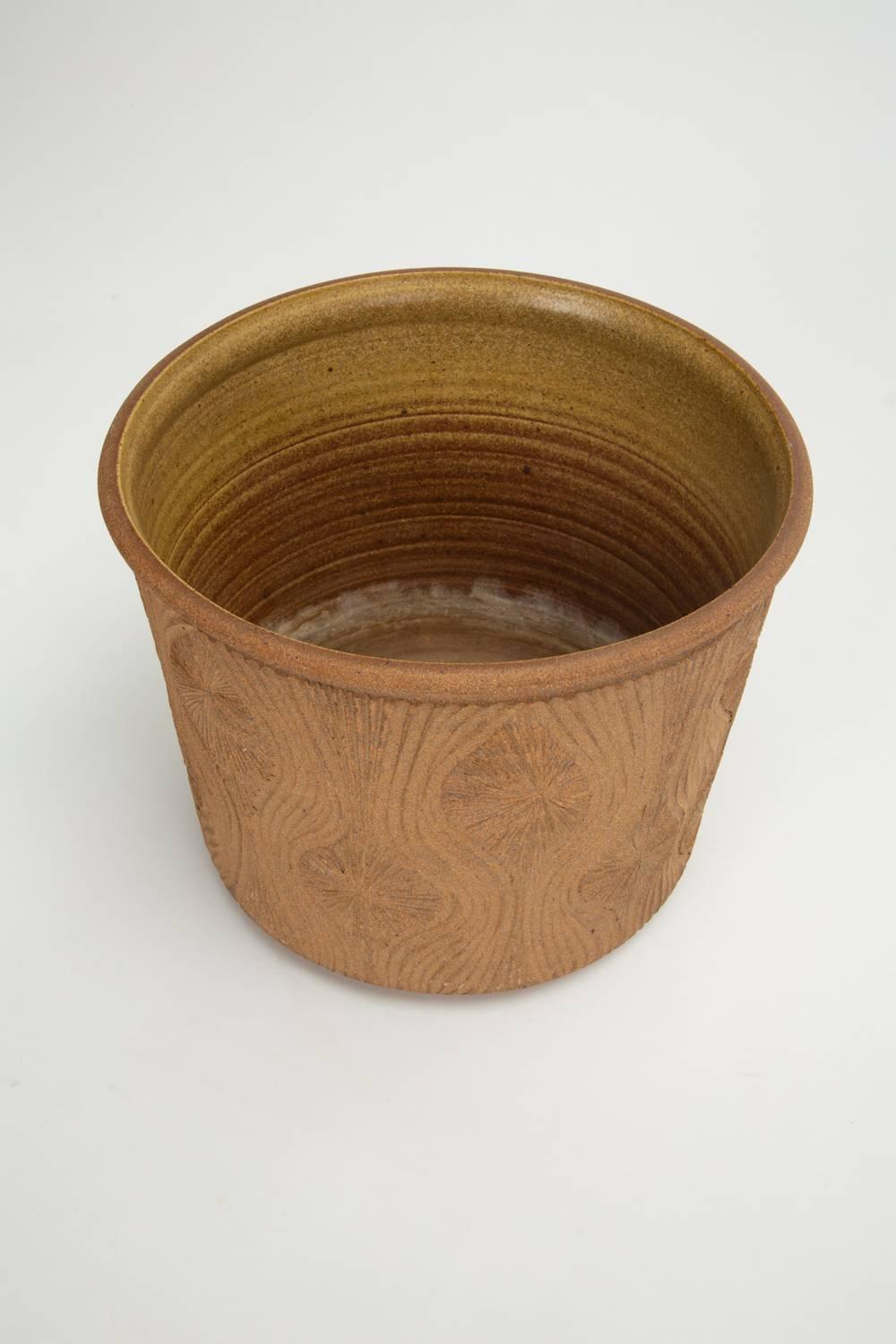 A 1970s handmade studio pottery planter by California ceramics artist Robert Maxwell. This example has a notched lip and cylindrical shape. It is hand incised with a Maxwell signature “teardrop sunburst” design. The interior of the planter is glazed