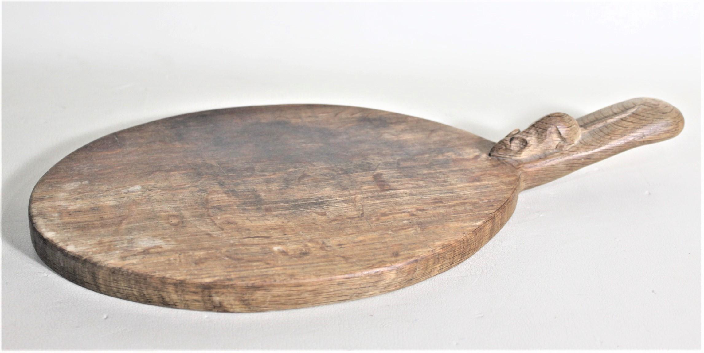 This solid oak oval cutting board was made by the renowned English furniture maker Robert 'Mouseman' Thompson in his signature Arts & Crafts style. The cutting board has a raised handle on one end with a hand carved mouse identifying it as being