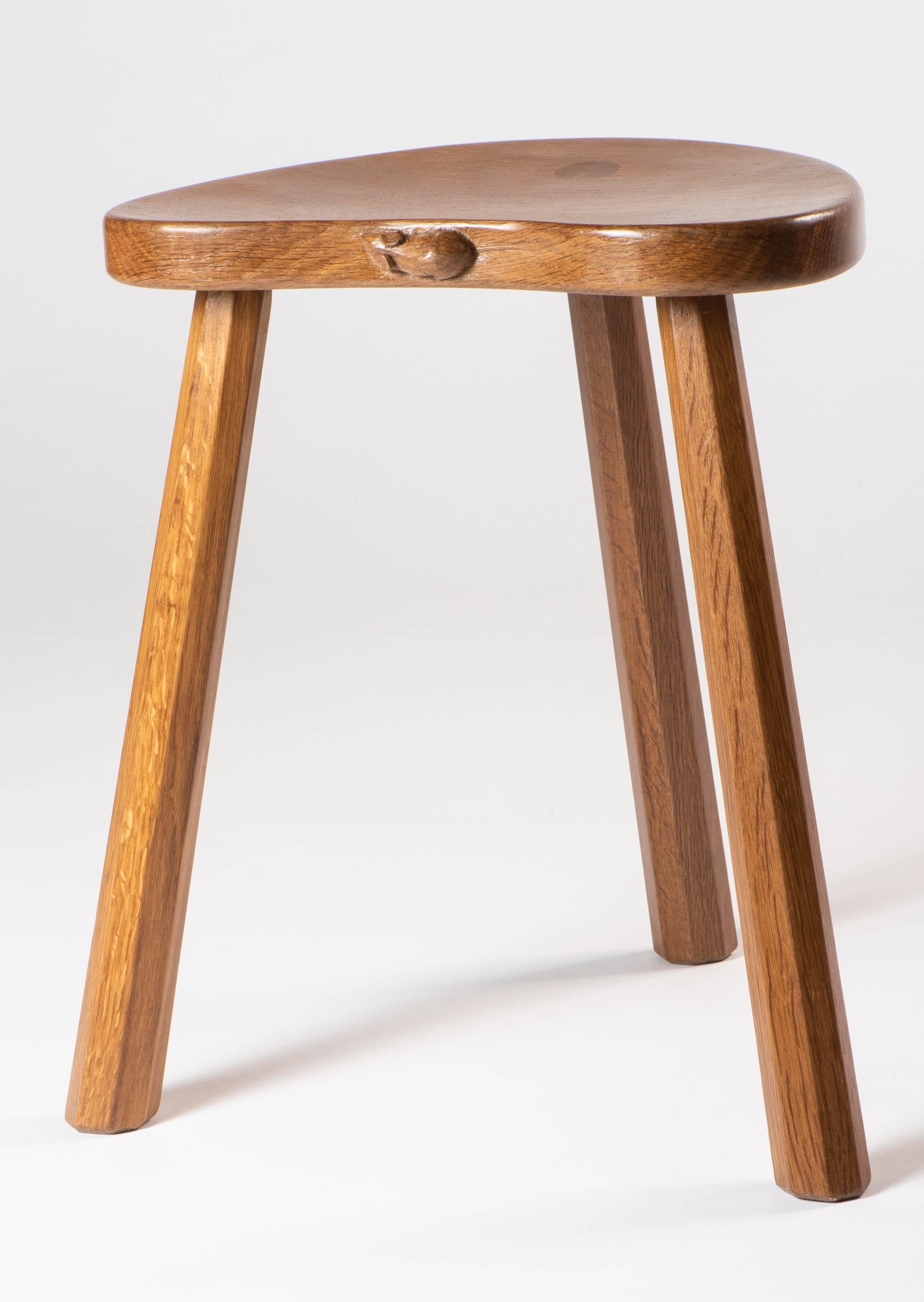 A Robert “Mouseman” Thompson milking stool.
Adzed kidney seat supported on octagonal legs.
Large dowels to the top.
Oak
Carved mouse 
English,
circa 1950.
 